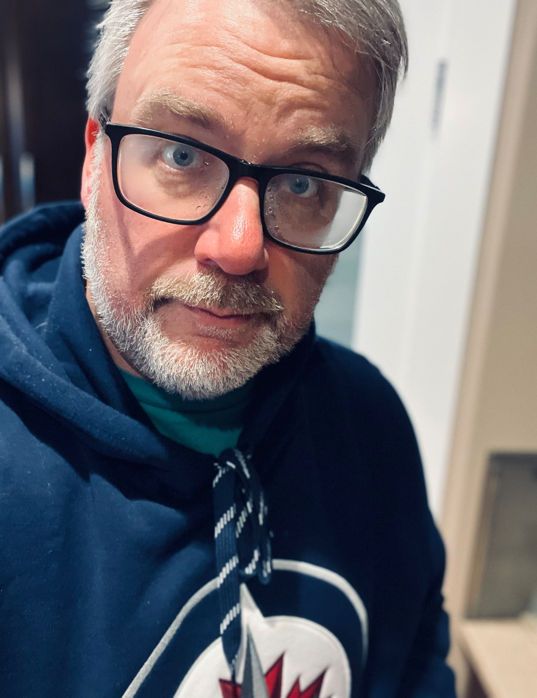 A person with glasses and a beard is wearing a navy hoodie with a design on the front.
