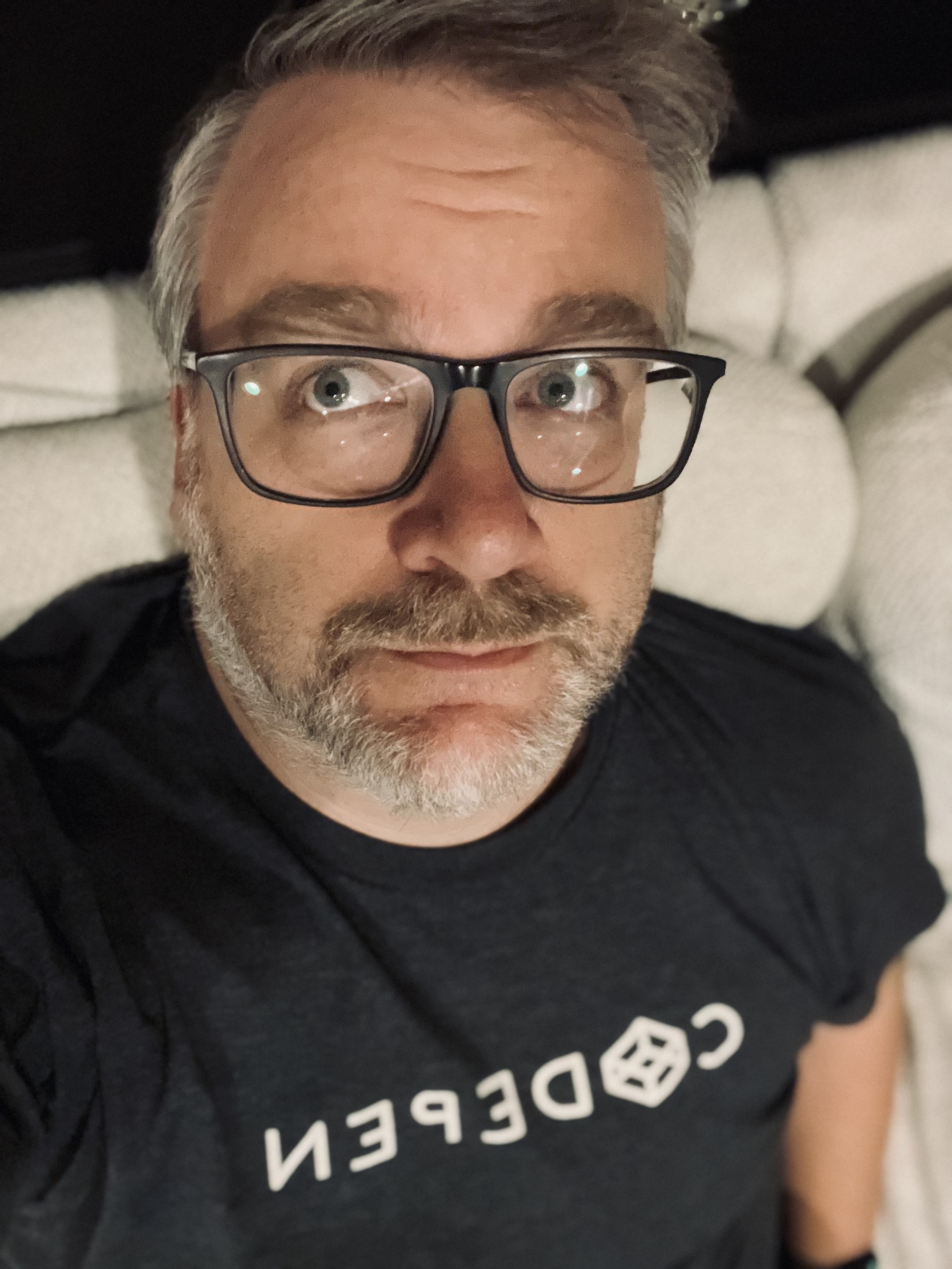 A person wearing glasses and a shirt with the word CODEPEN featuring a cube logo is looking upwards.