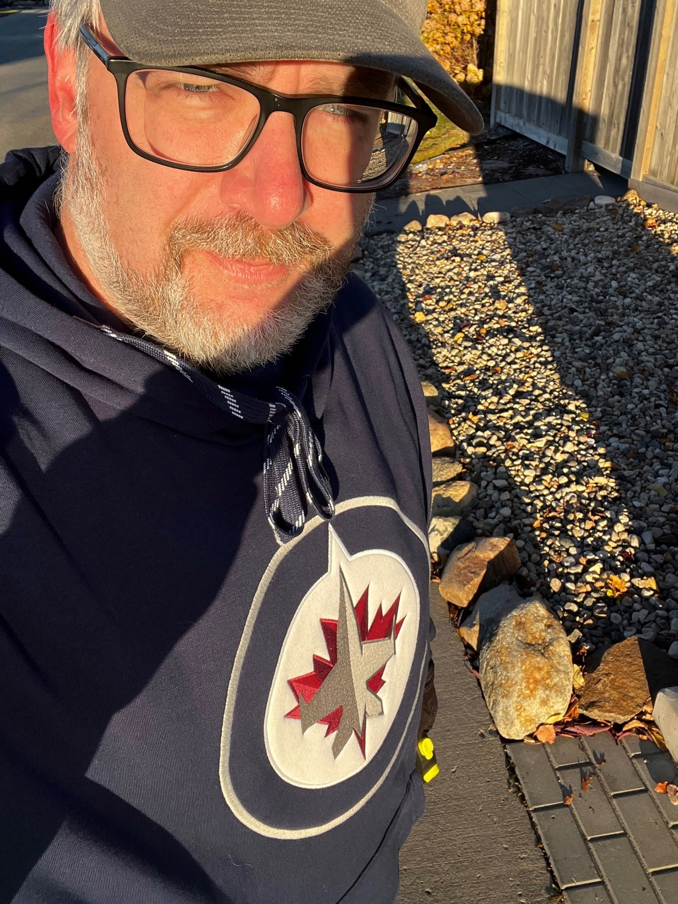Seflie of me with a Winnipeg Jets bunnyhug / hoodie on. I’m squinting into the sun on a walk outside.