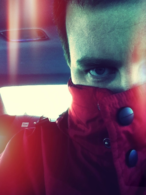 A person is partially covering their face with a red jacket inside a dimly lit vehicle.