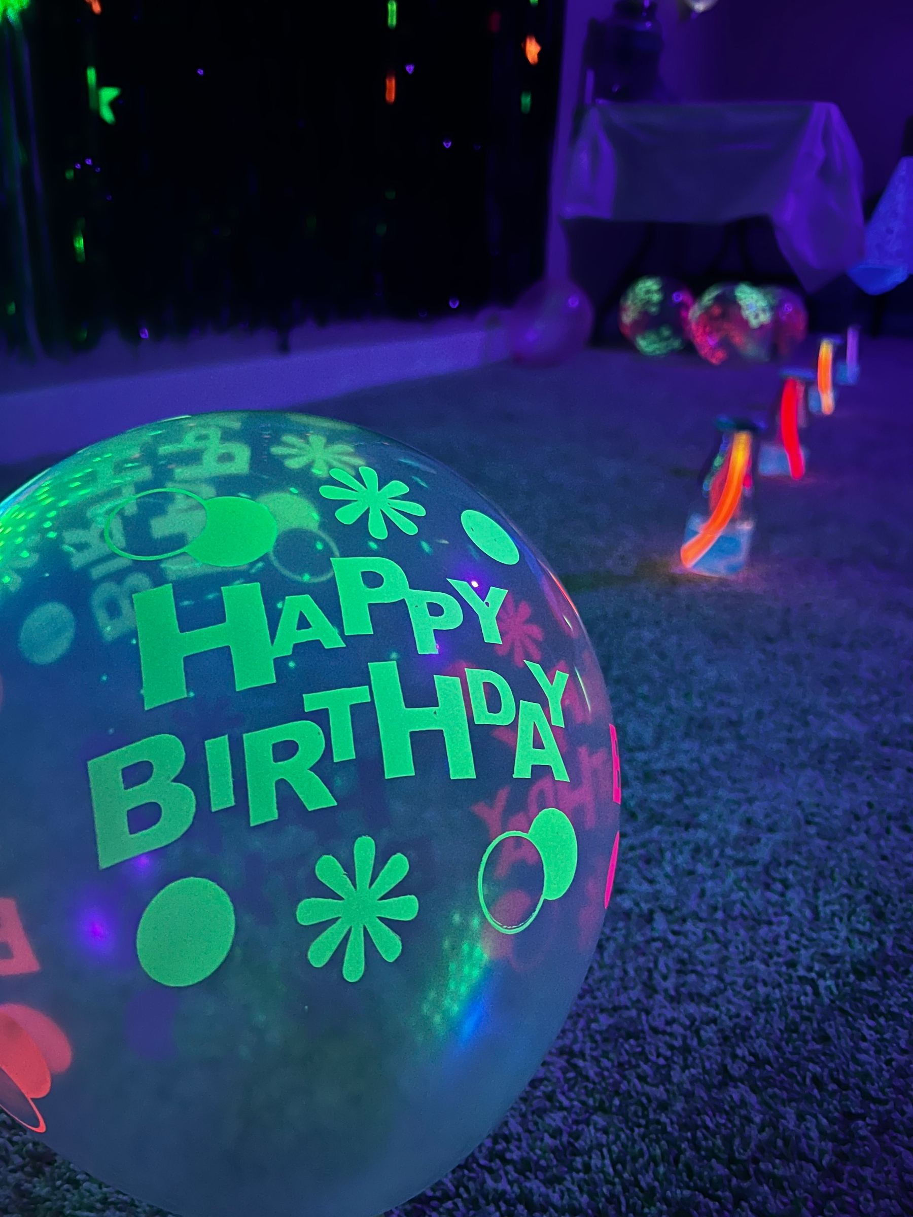 A glowing balloon with Happy Birthday printed on it is set against a festive, dimly lit room with colorful lights.