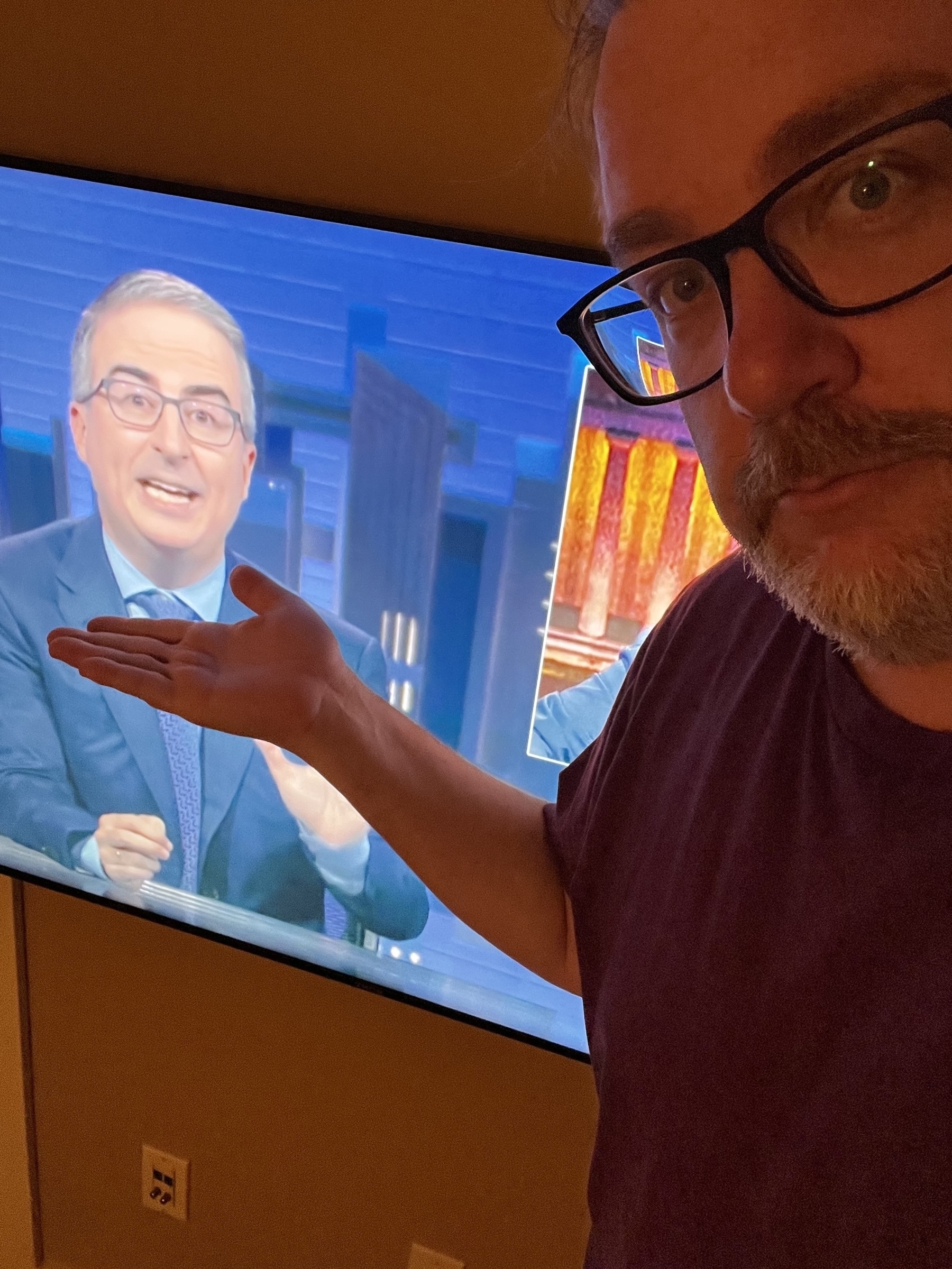 A person gestures toward a television screen displaying a man in a suit.