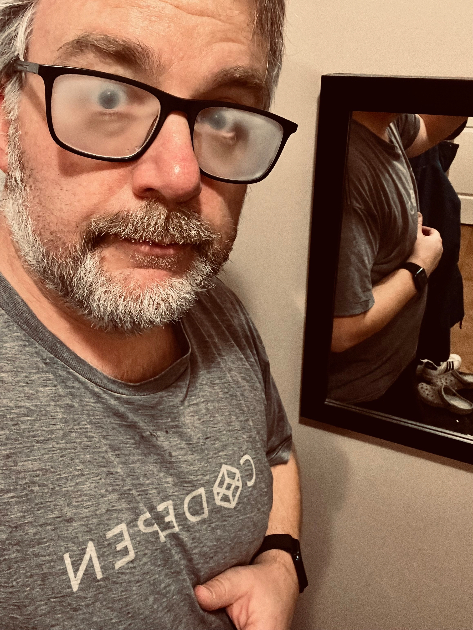 A man with foggy glasses, wearing a gray CODEPEN shirt, is posing in front of a mirror.