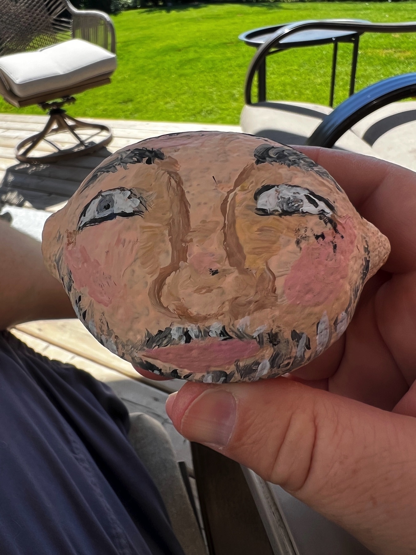 A hand is holding a painted lemon with a face design, depicting features like eyes, a nose, and a mouth.