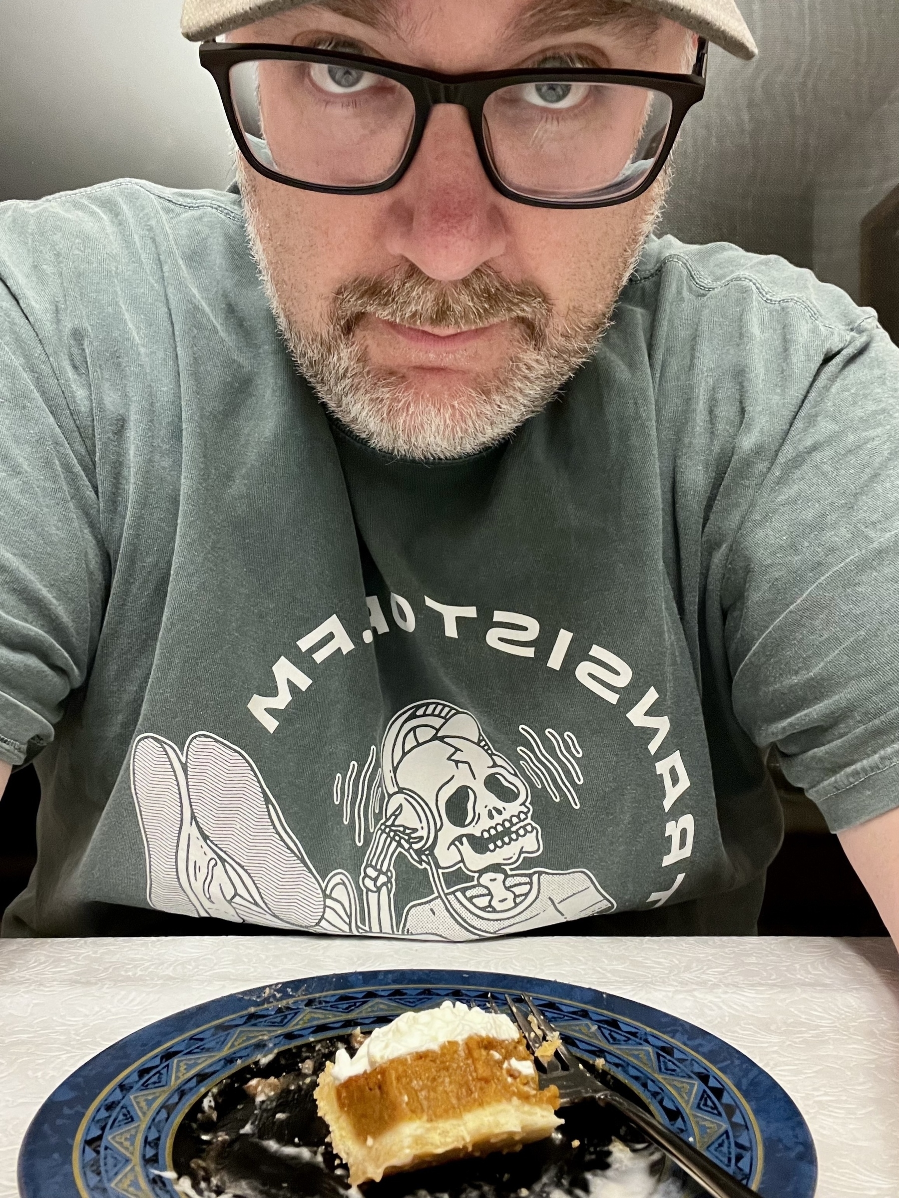 A person with glasses and a beard is seated at a table with a partially eaten slice of pie on a decorative plate.