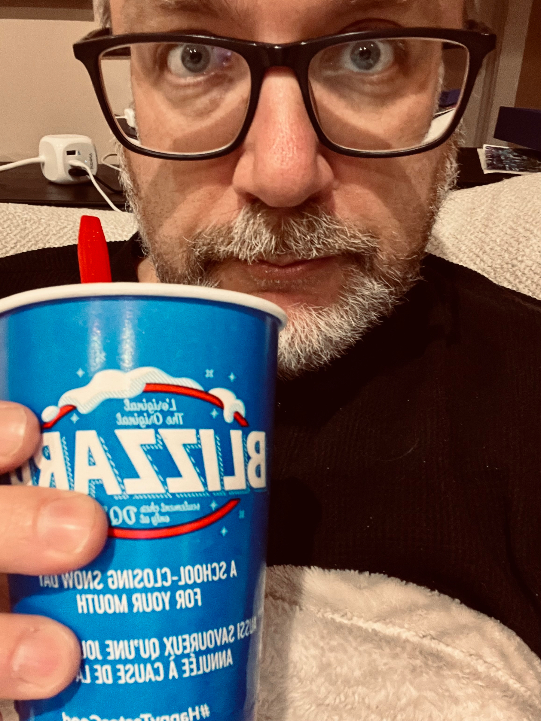 A person wearing glasses holds a blue Blizzard cup close to their face while sitting on a couch.