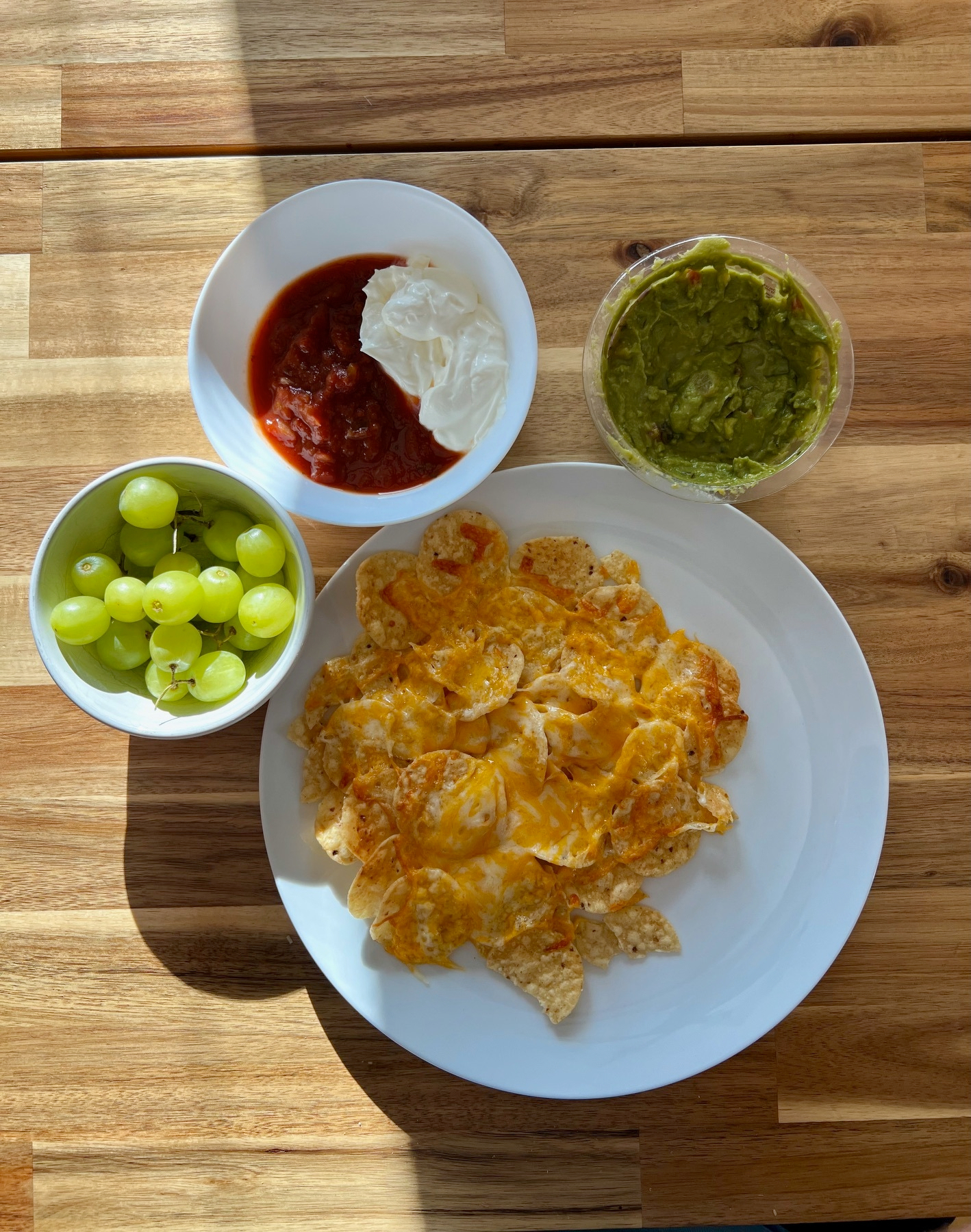 Photo of a plate of nachos with salsa, sour cream, and guacamole beside it in bowls.