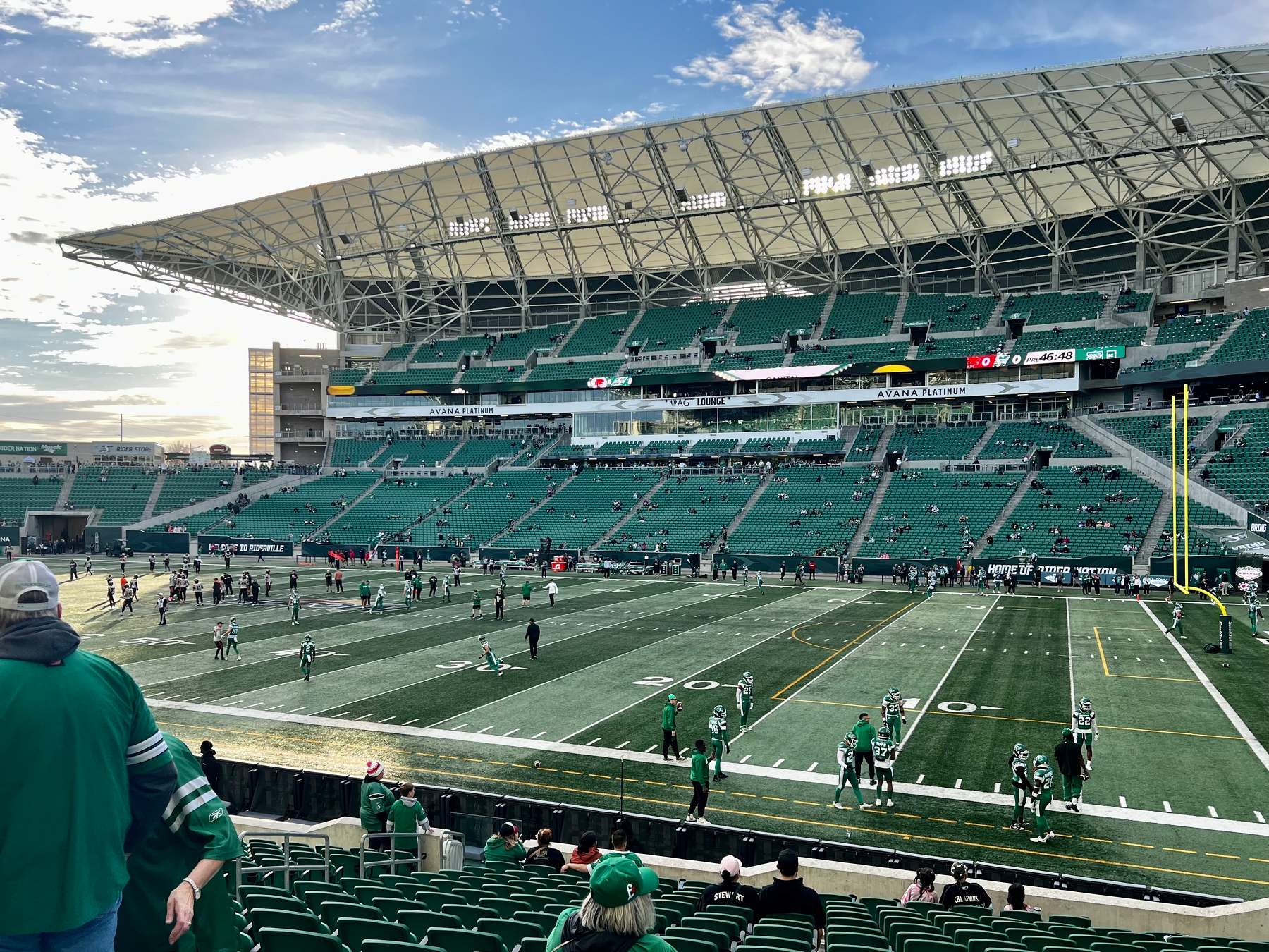 A football stadium with a green field is hosting a game as players and spectators are present.