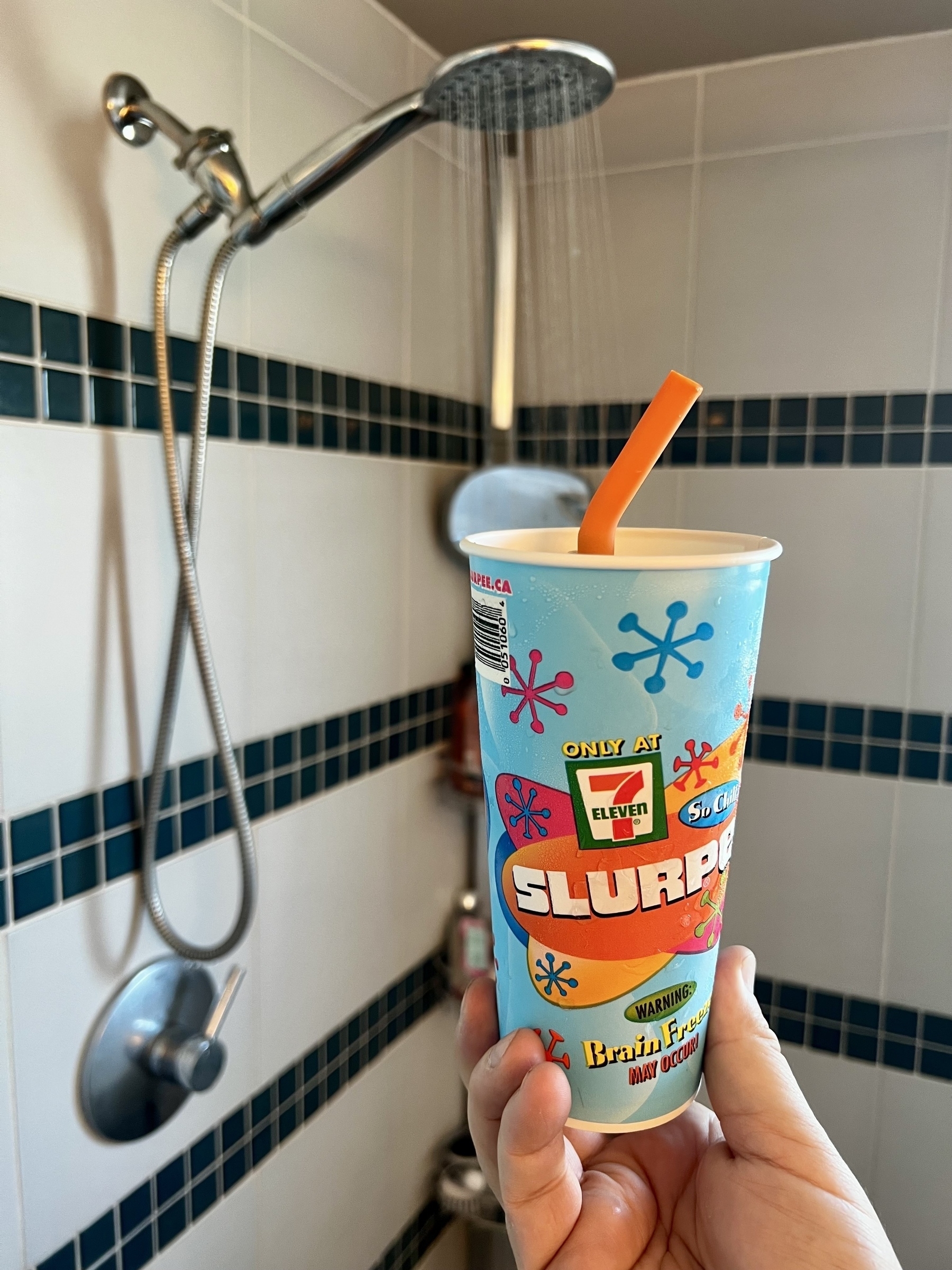 A Slurpee is held in a hand while a shower runs in the background. 