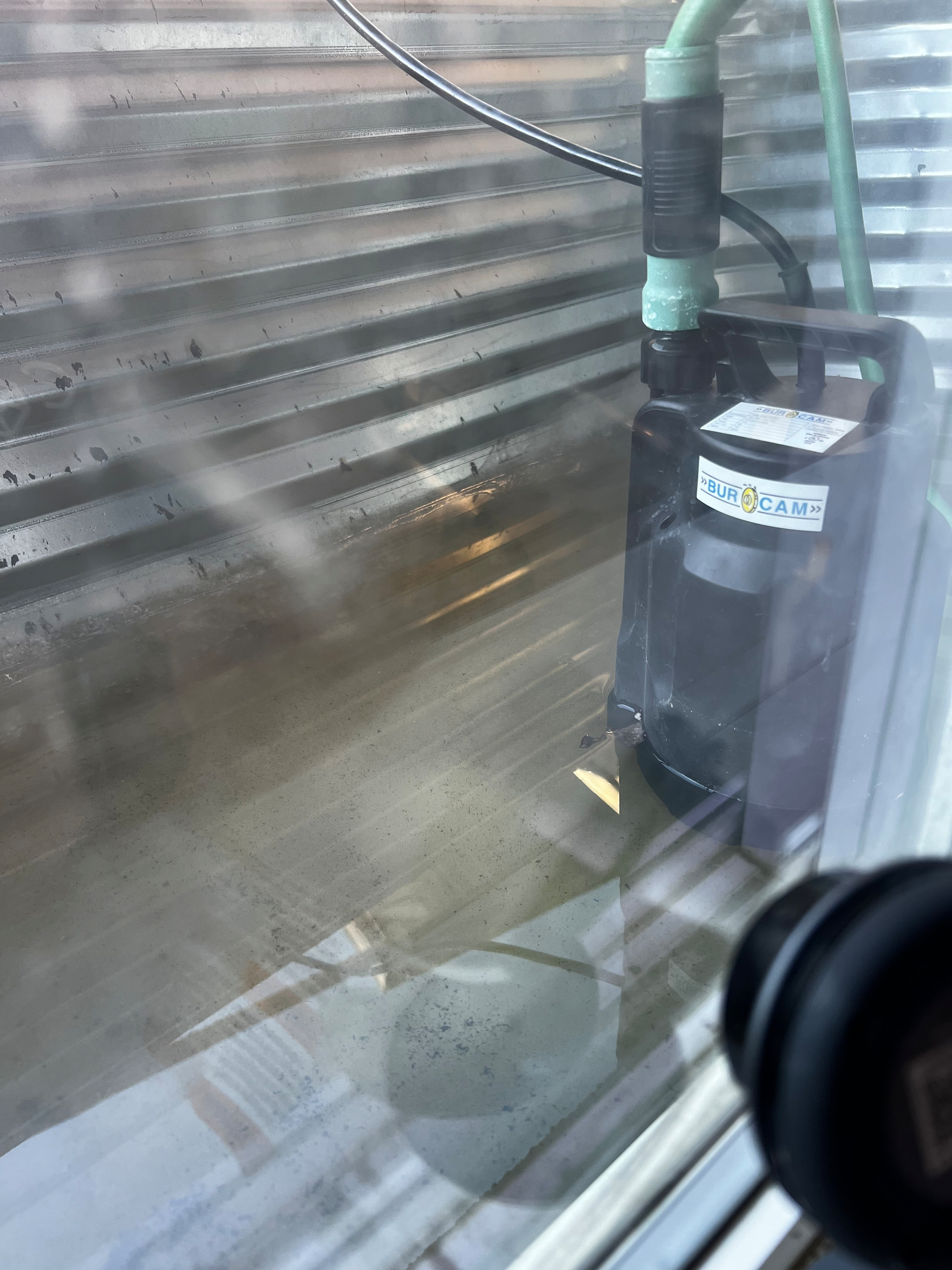 A submersible pump is placed inside a partially filled stainless steel water tank.