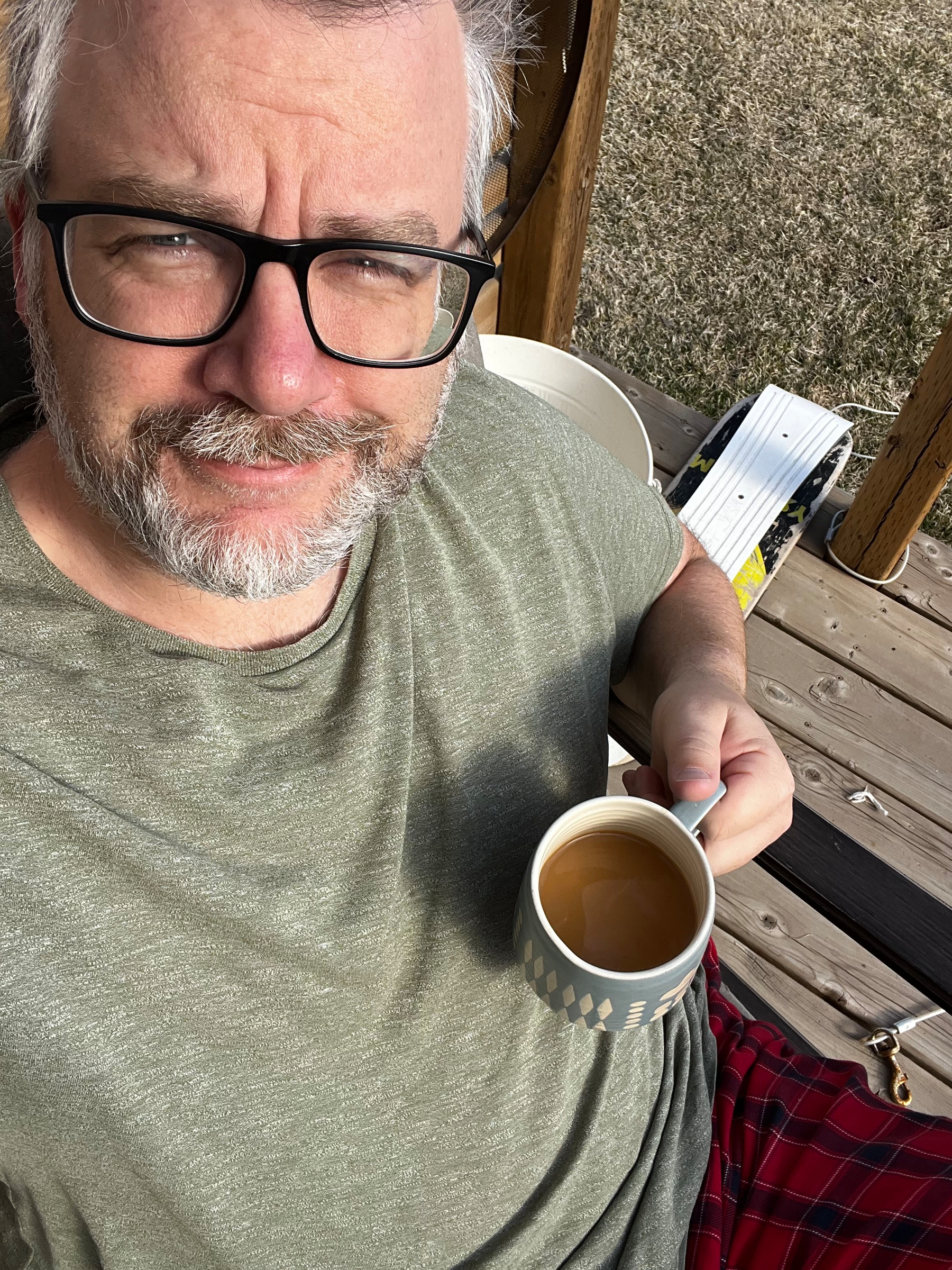 A person with glasses is sitting on a wooden surface, holding a polka dot mug with a beverage inside.