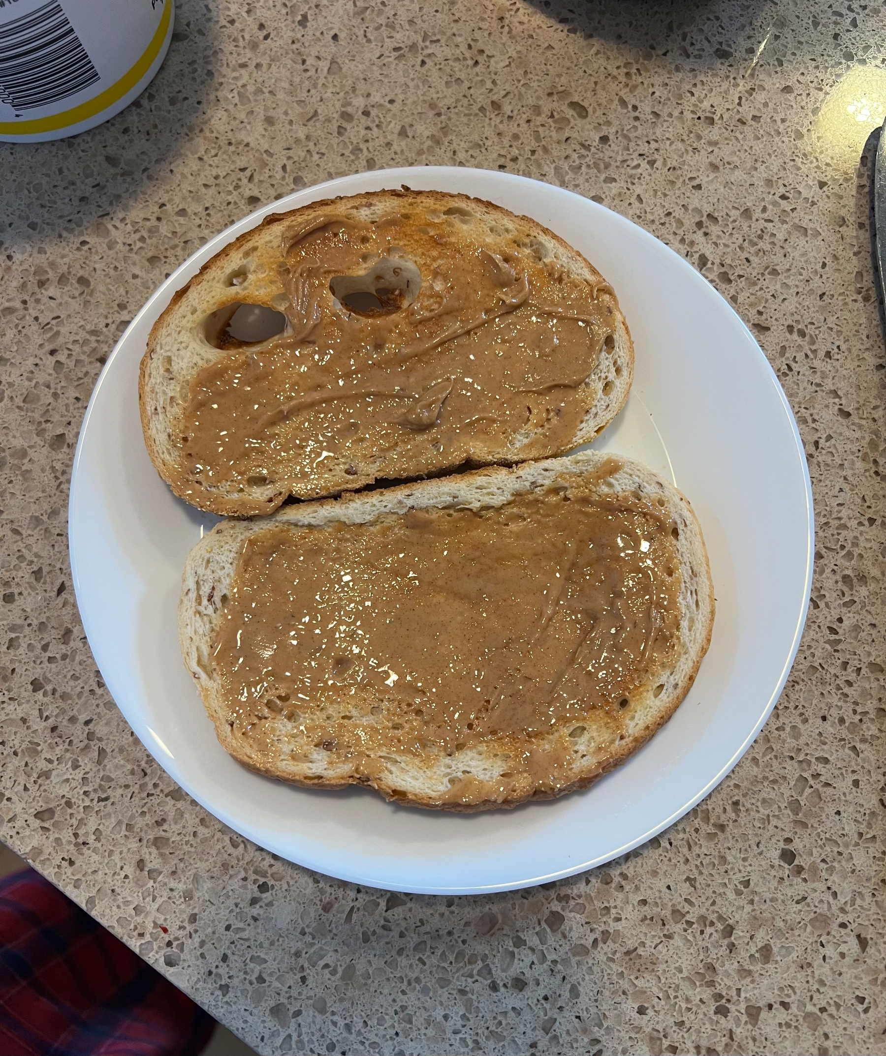 Two slices of toasted bread spread with peanut butter are placed on a white plate.