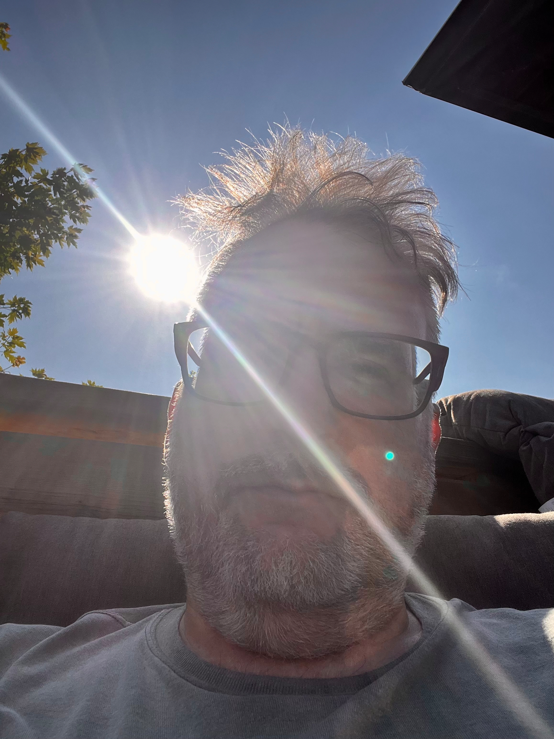 A man wearing glasses is sitting outdoors with the sun shining brightly behind him, creating lens flare effects.