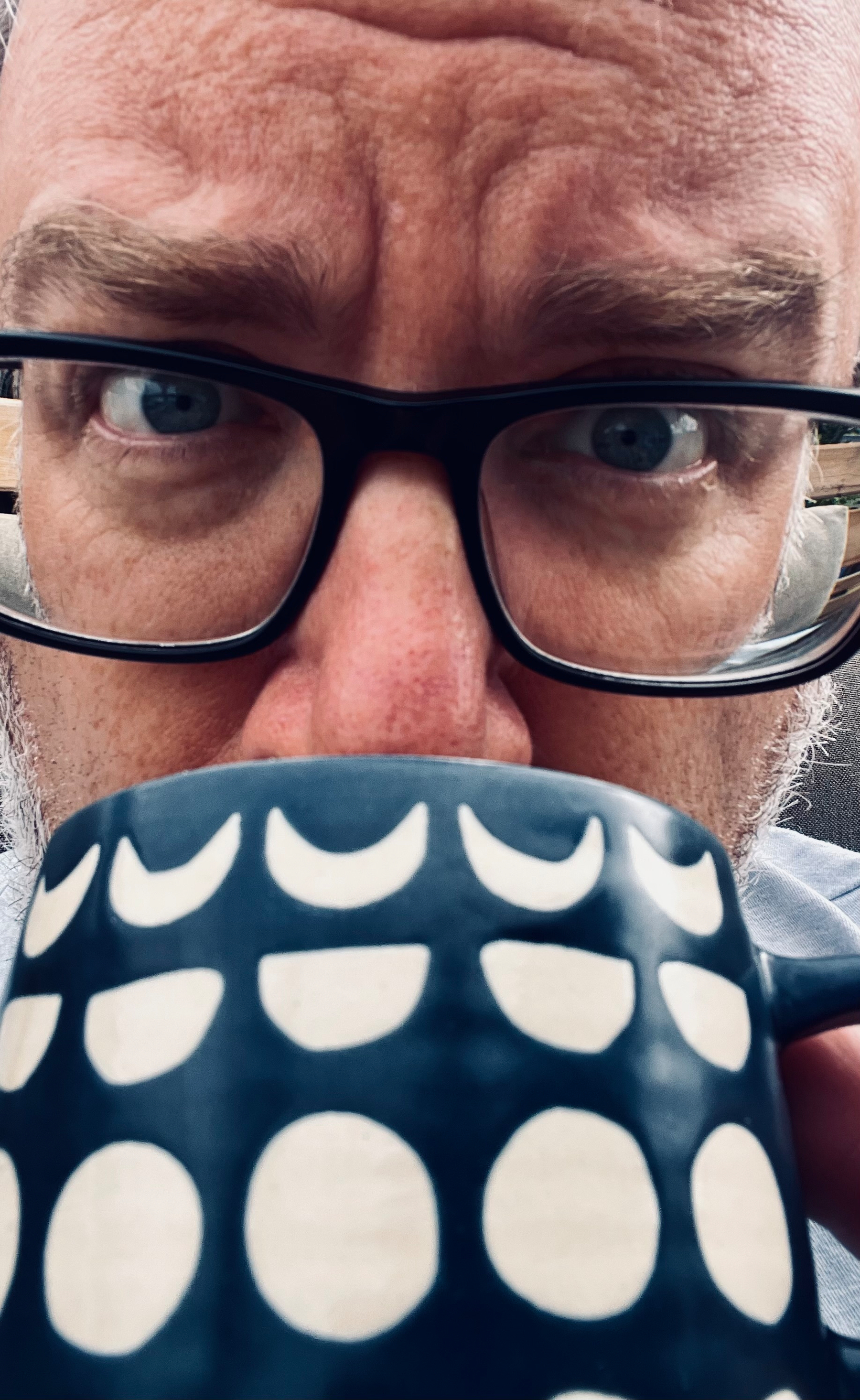 A person wearing glasses is closely holding and drinking from a dark blue mug with white geometric patterns.