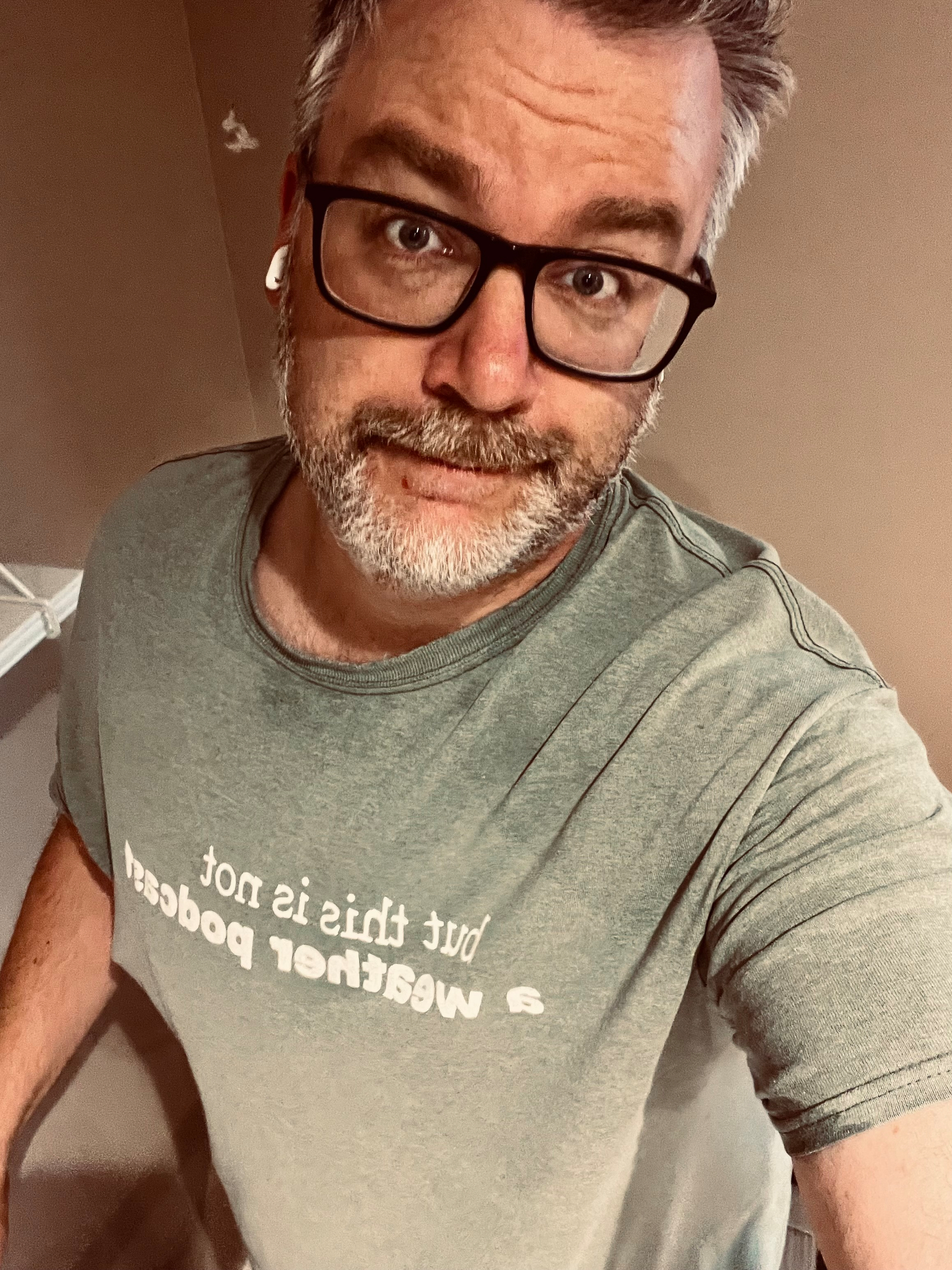 A person with glasses and earphones is wearing a T-shirt that says, But this is not a Weather Podcast.