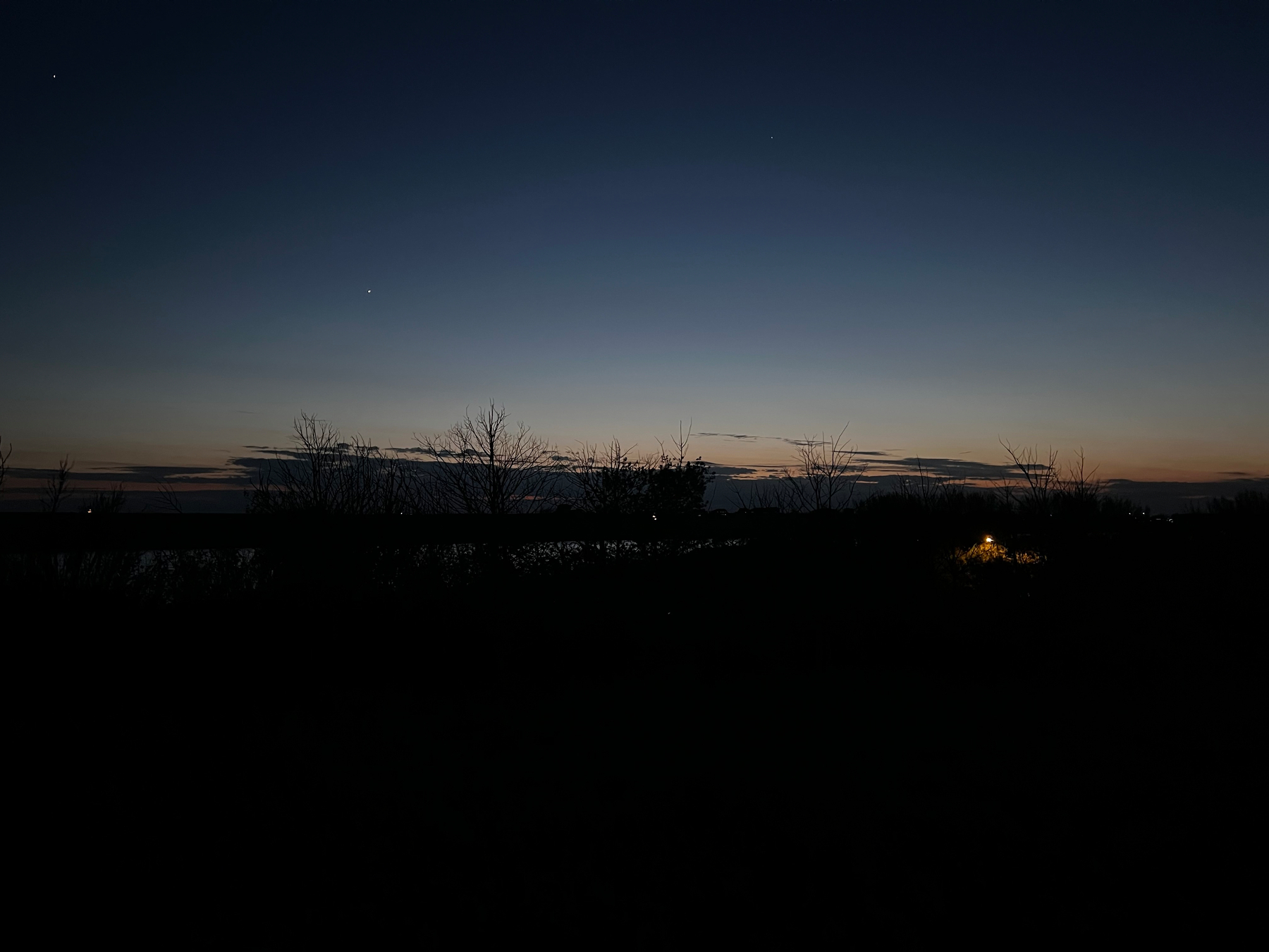 A serene twilight sky with silhouettes of trees and a warm light glowing in the distance.