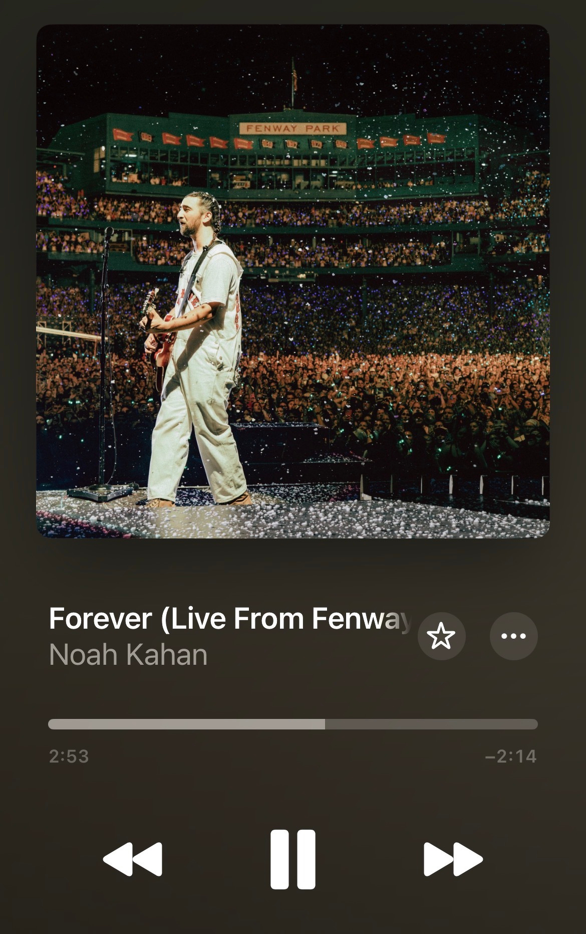 Noah Kahan performs on stage at Fenway Park in front of a large, cheering crowd, with colorful lights illuminating the scene.