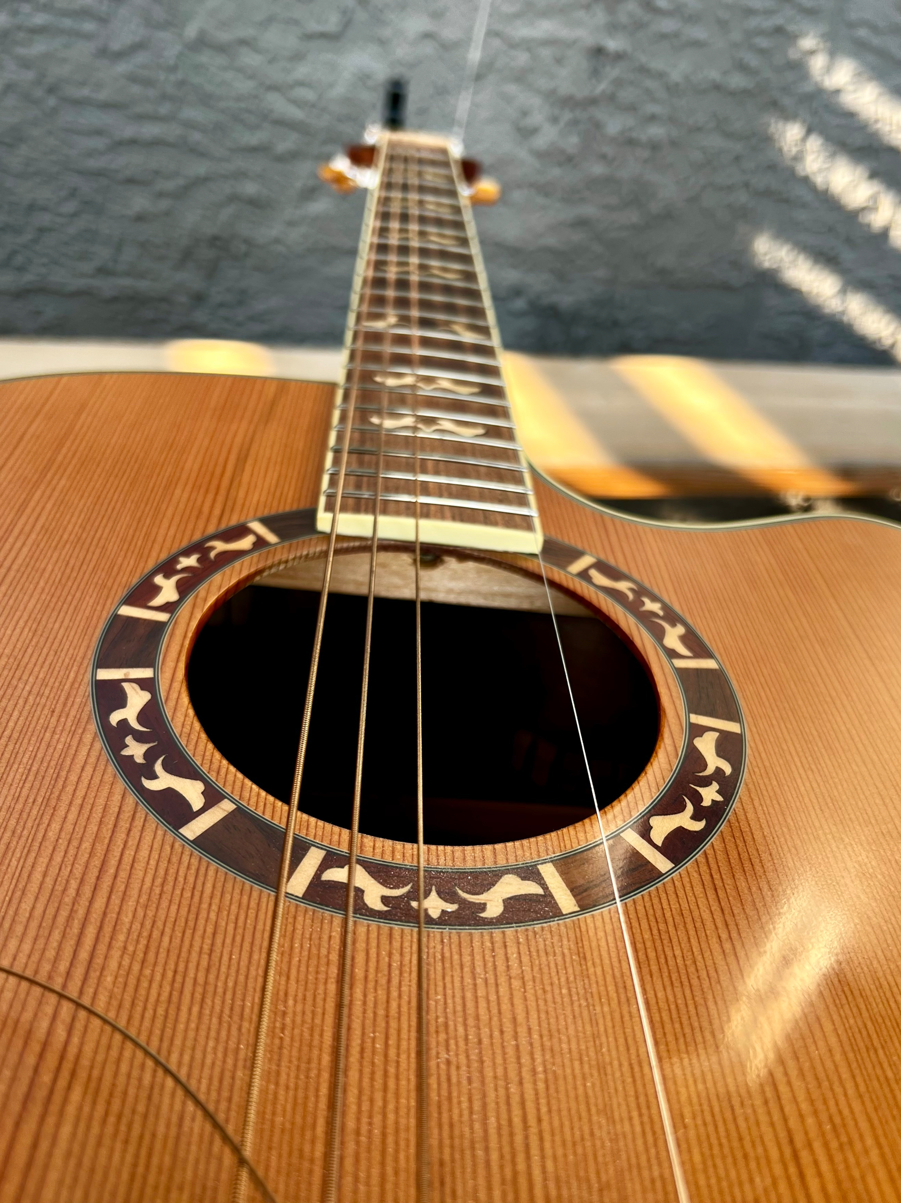 An acoustic guitar with detailed inlays around the soundhole is shown from a close-up perspective along its strings and fretboard.
