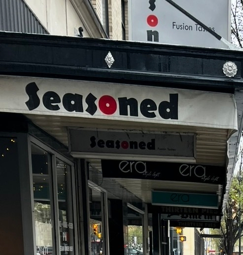 A street features shop signs for Seasoned and era along with the phrase Fusion Tastes.