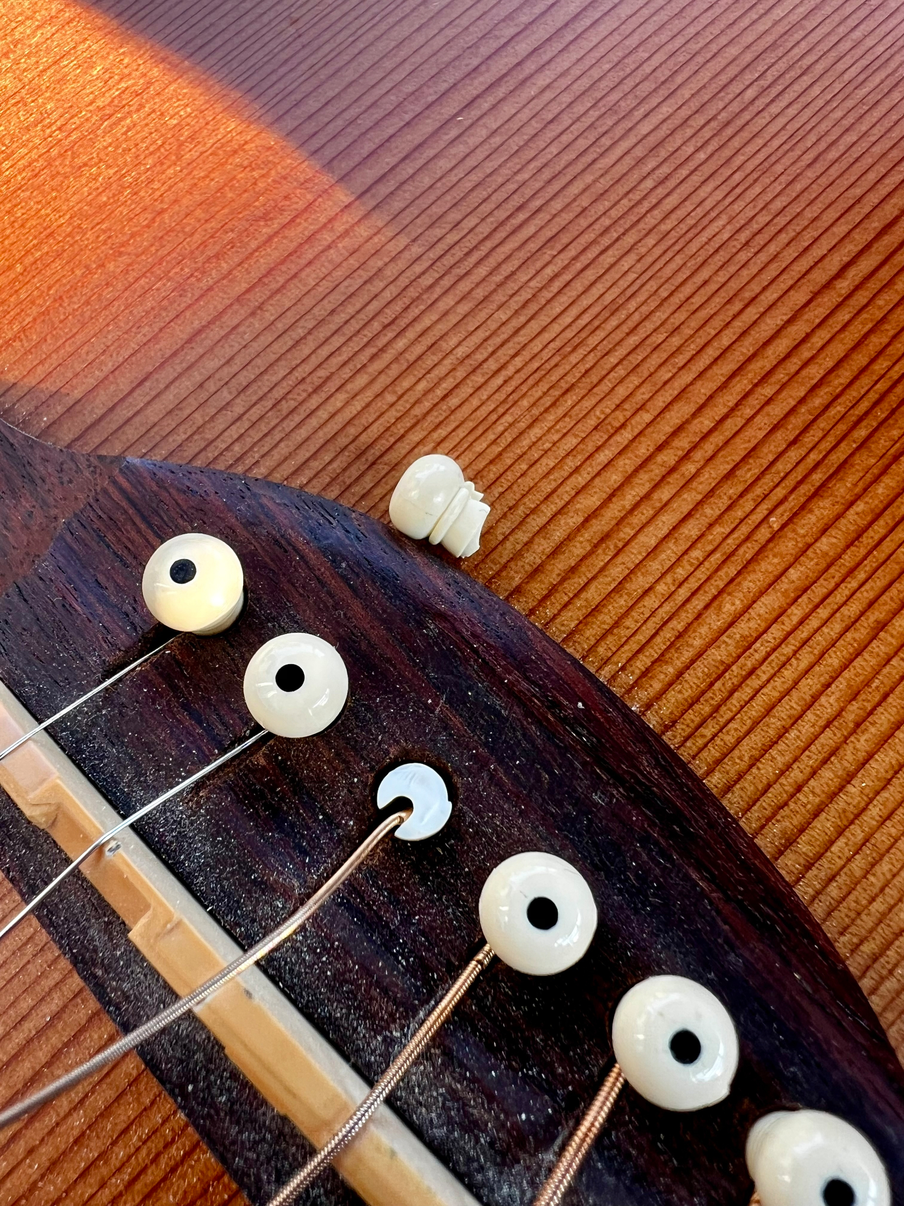 A close-up view of an acoustic guitar's bridge with one loose or broken bridge pin lying on the guitar's wooden body.