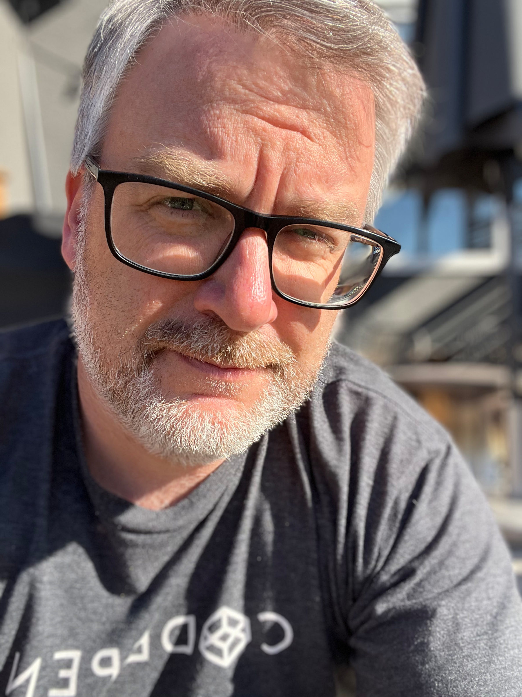 A man with glasses and a beard is wearing a T-shirt and looking at the camera.
