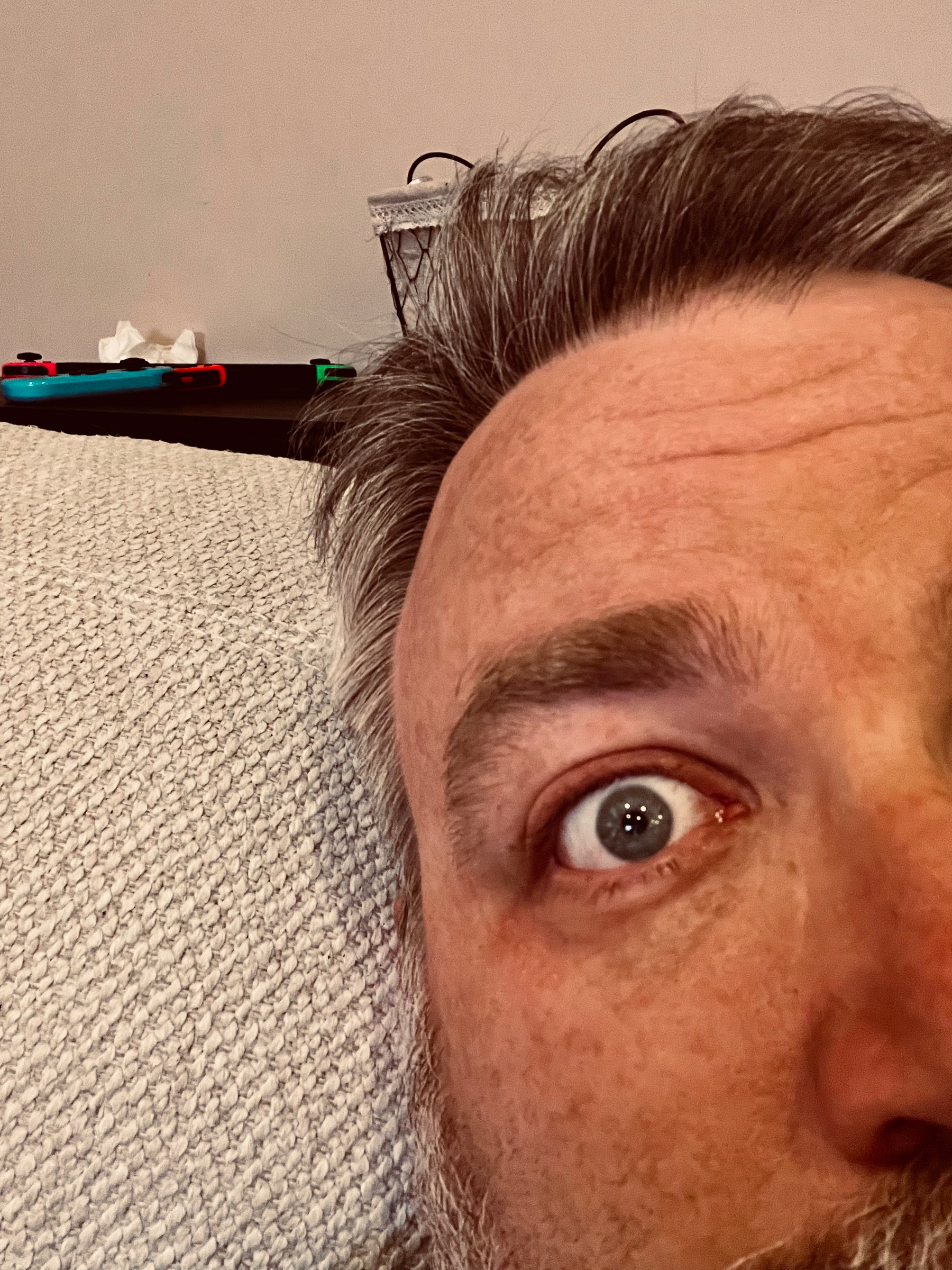 A close-up shows a person's face with one eye wide open, lying on a textured surface with a few items in the background.