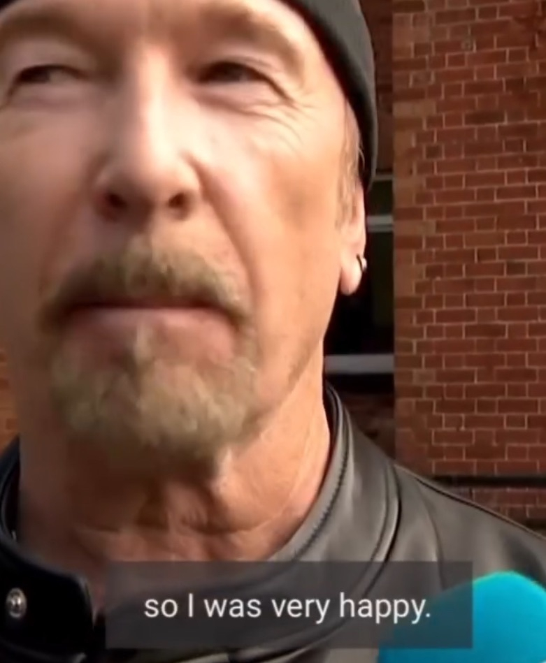 A man with a beard and an earring is wearing a black cap and leather jacket, speaking with a subtitle that reads so I was very happy.