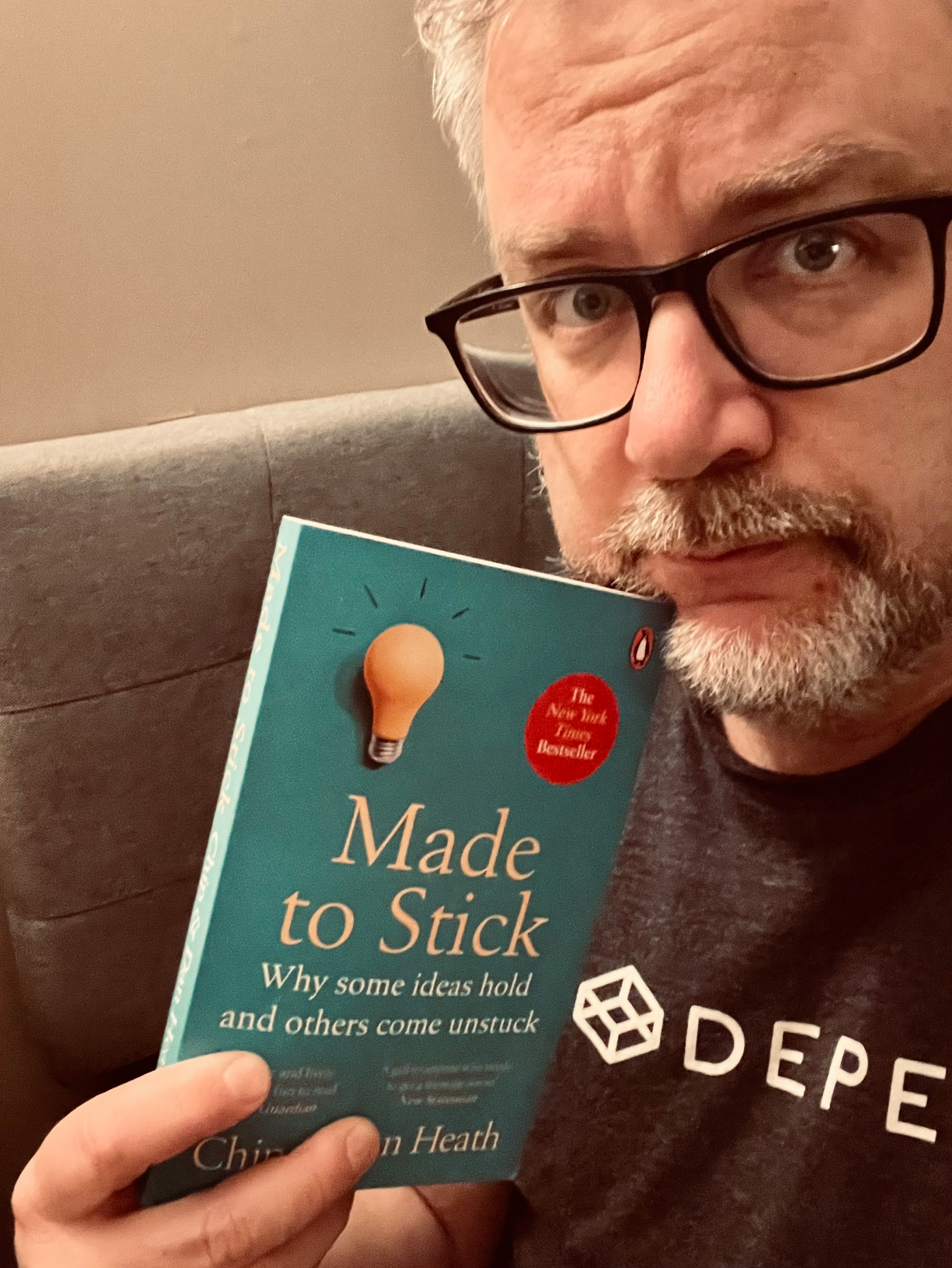 A person wearing glasses holds the book Made to Stick by Chip and Dan Heath.