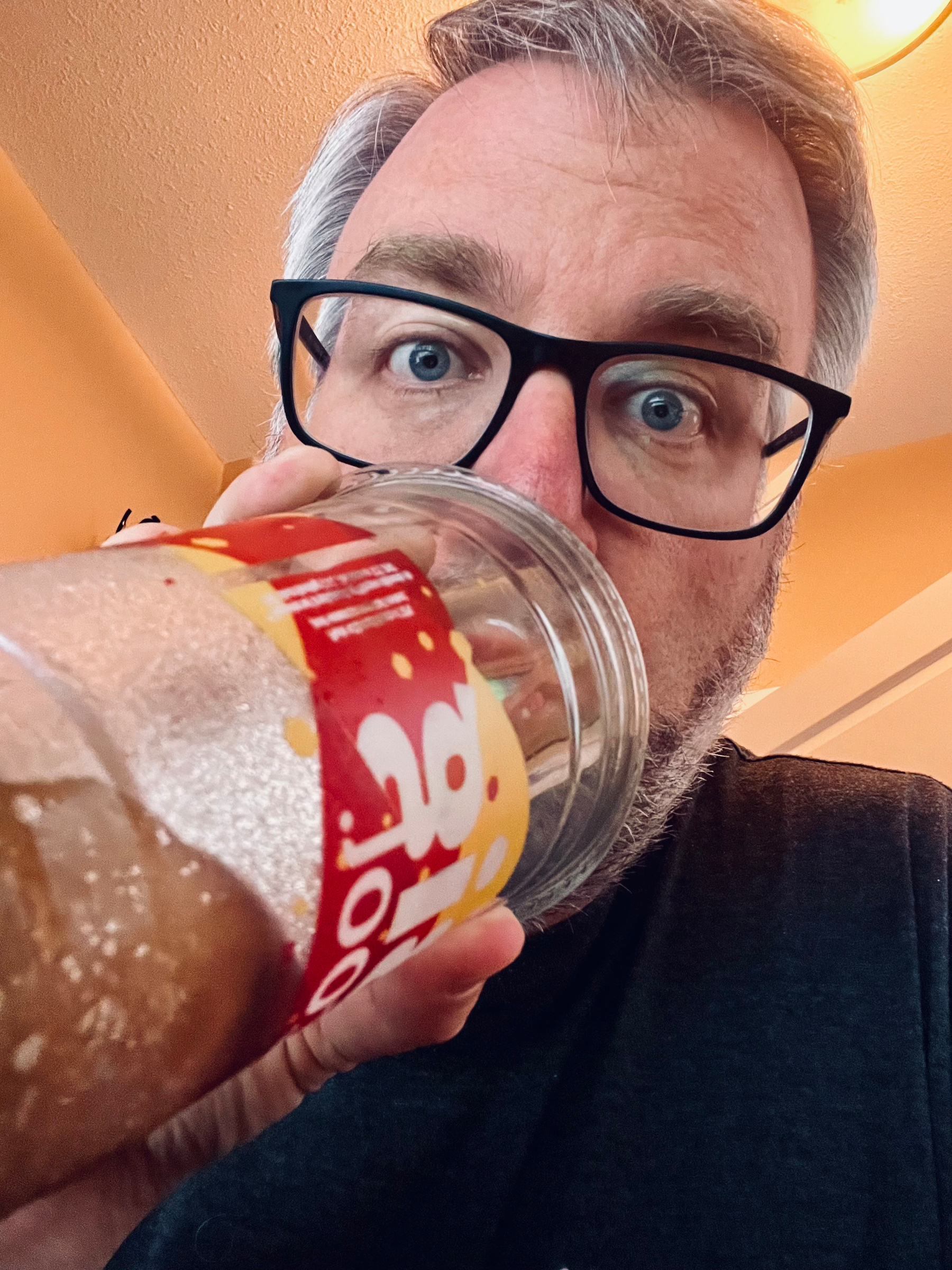 A person wearing glasses is drinking from a large slurpee with a straw.