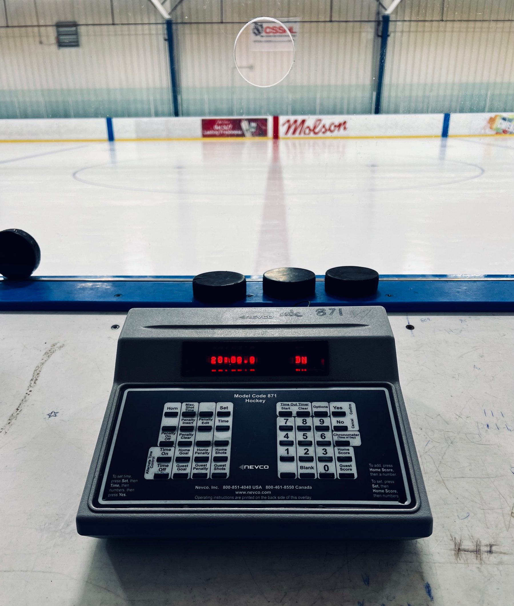 A hockey rink is viewed from the perspective of a scoreboard control panel in an empty arena.