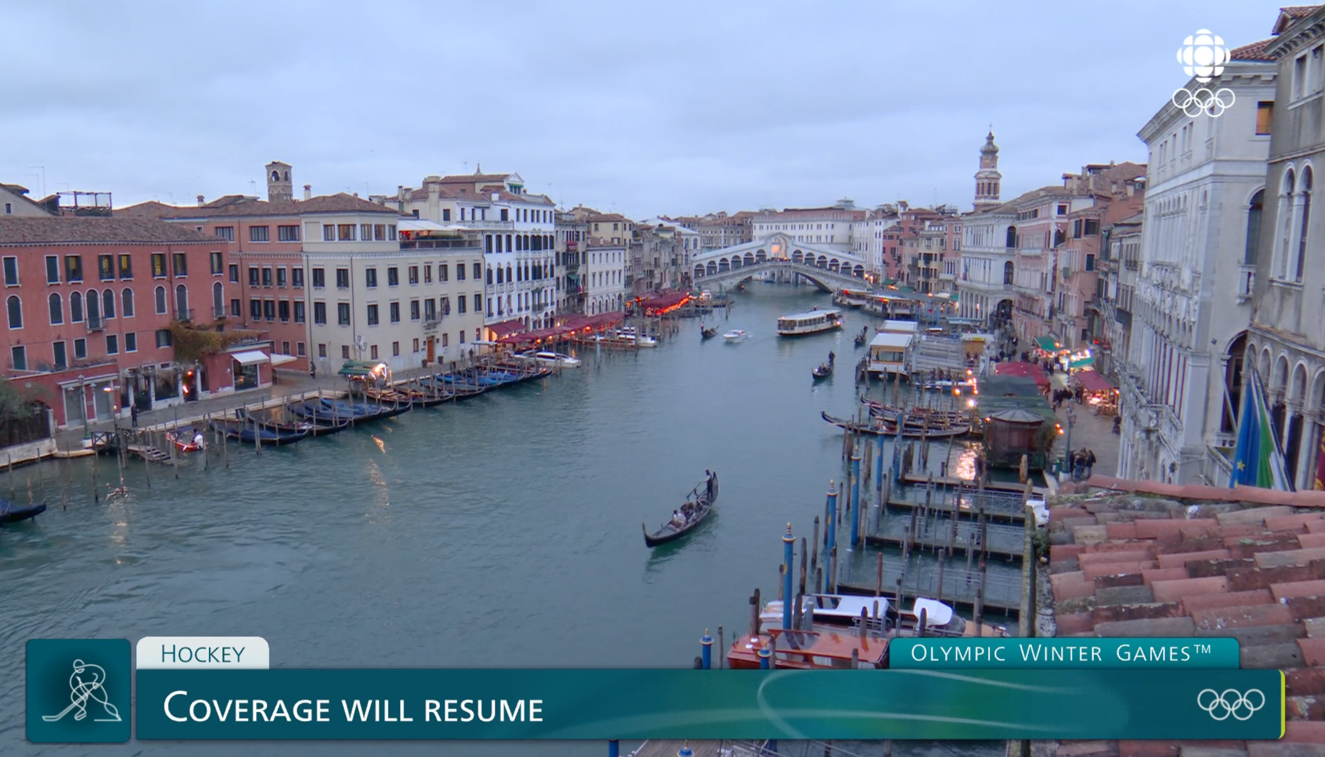 A canal in a European city with boats and historic buildings lines each side, accompanied by a text overlay about Olympic Winter Games coverage.