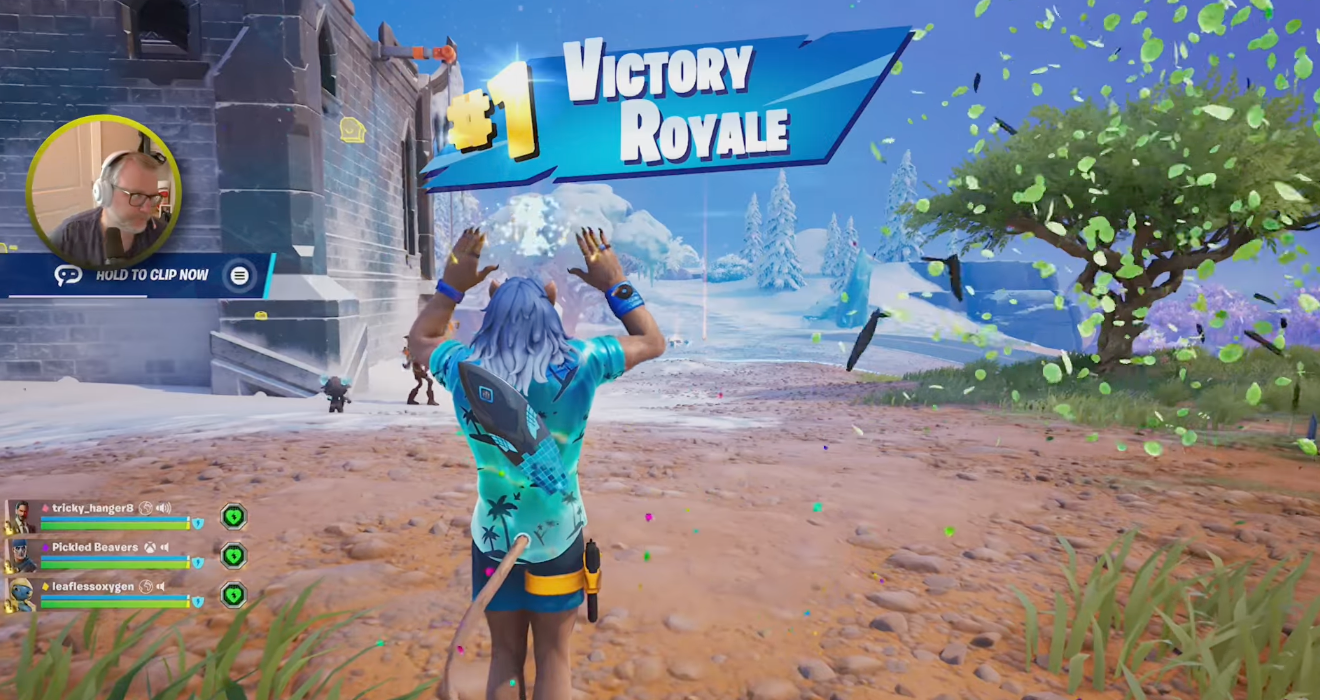 A character in a video game is celebrating a Victory Royale win while confetti falls, and a small streamer window appears in the corner.