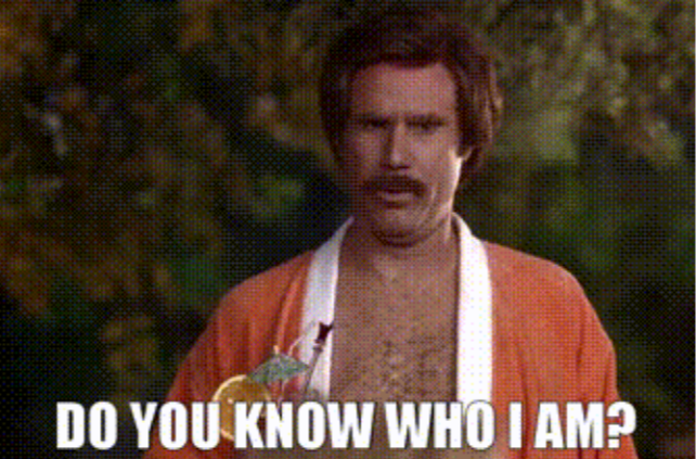 Will Ferrell as Ron Burgandy in Anchorman with a mustache wearing an orange robe is holding a drink and asking, Do you know who I am?
