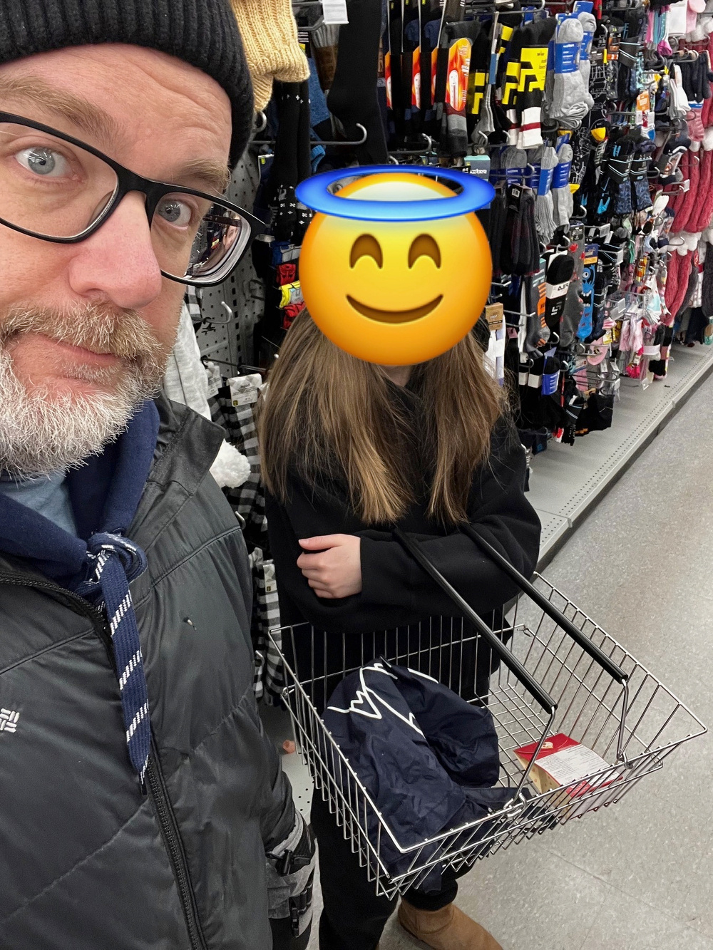 Two people are shopping in a store aisle filled with socks and accessories, with one person's face replaced by an emoji.