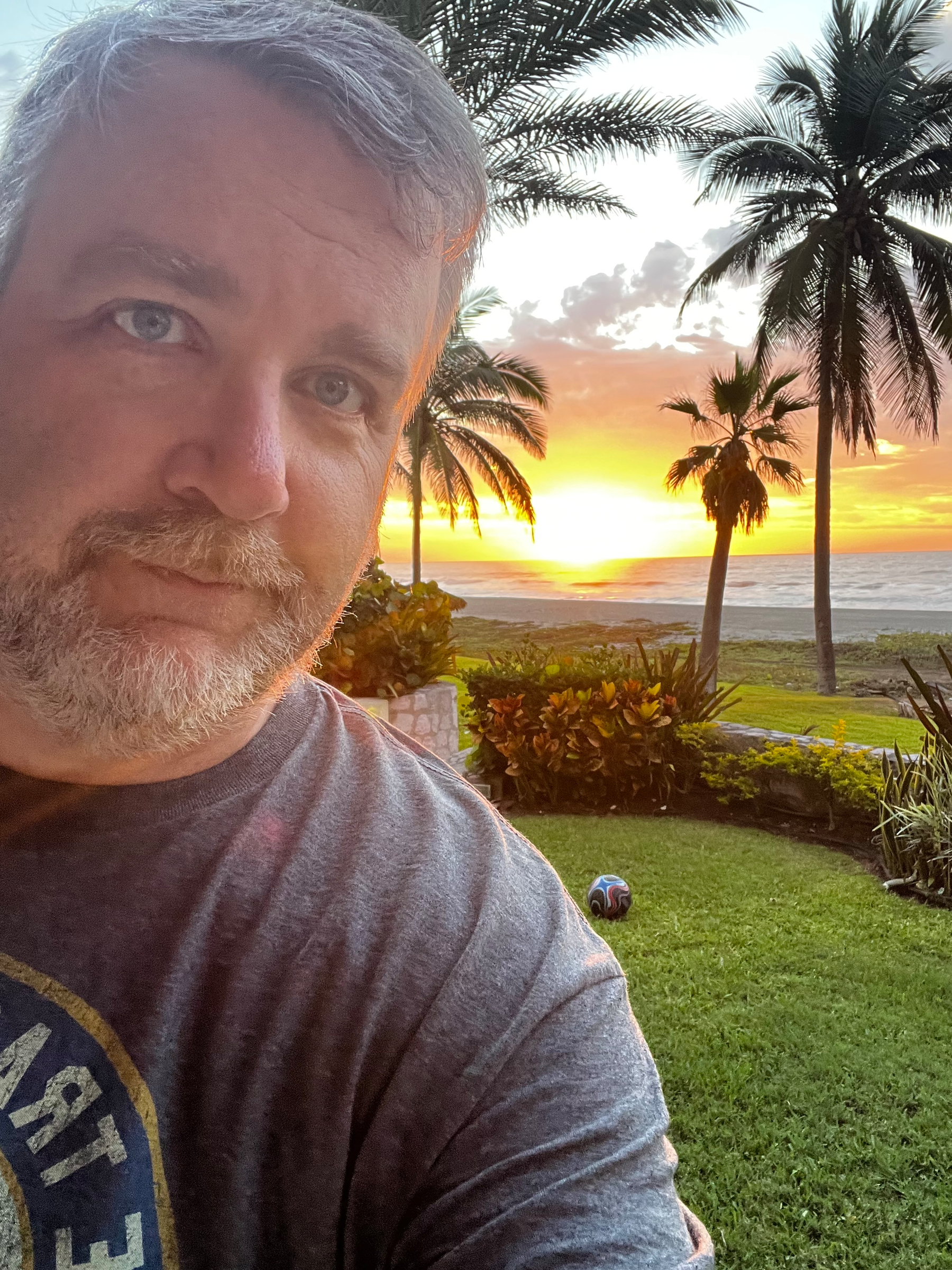 I’m posing for a selfie with a vibrant sunset and palm trees in the background.