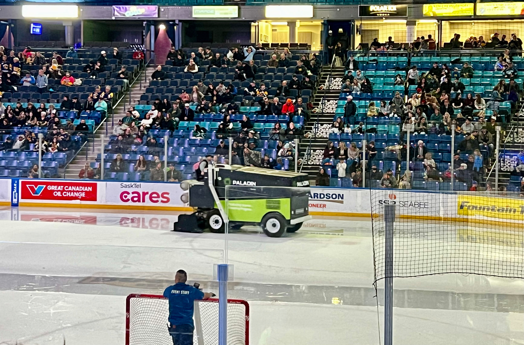 A Zamboni is resurfacing the ice in a hockey arena with many spectators in the stands.