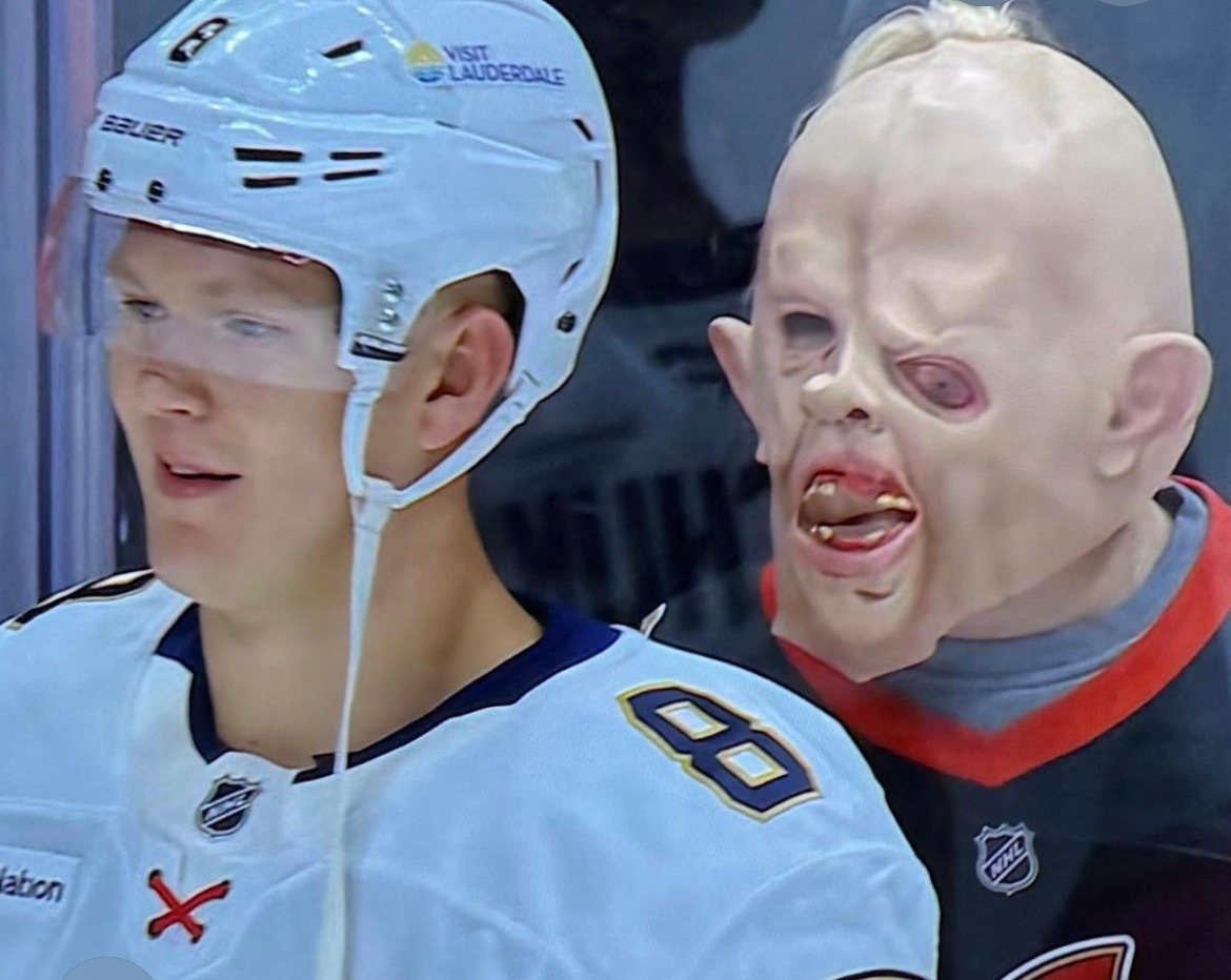 A hockey player in full gear stands next to a person wearing a grotesque mask with distorted facial features.