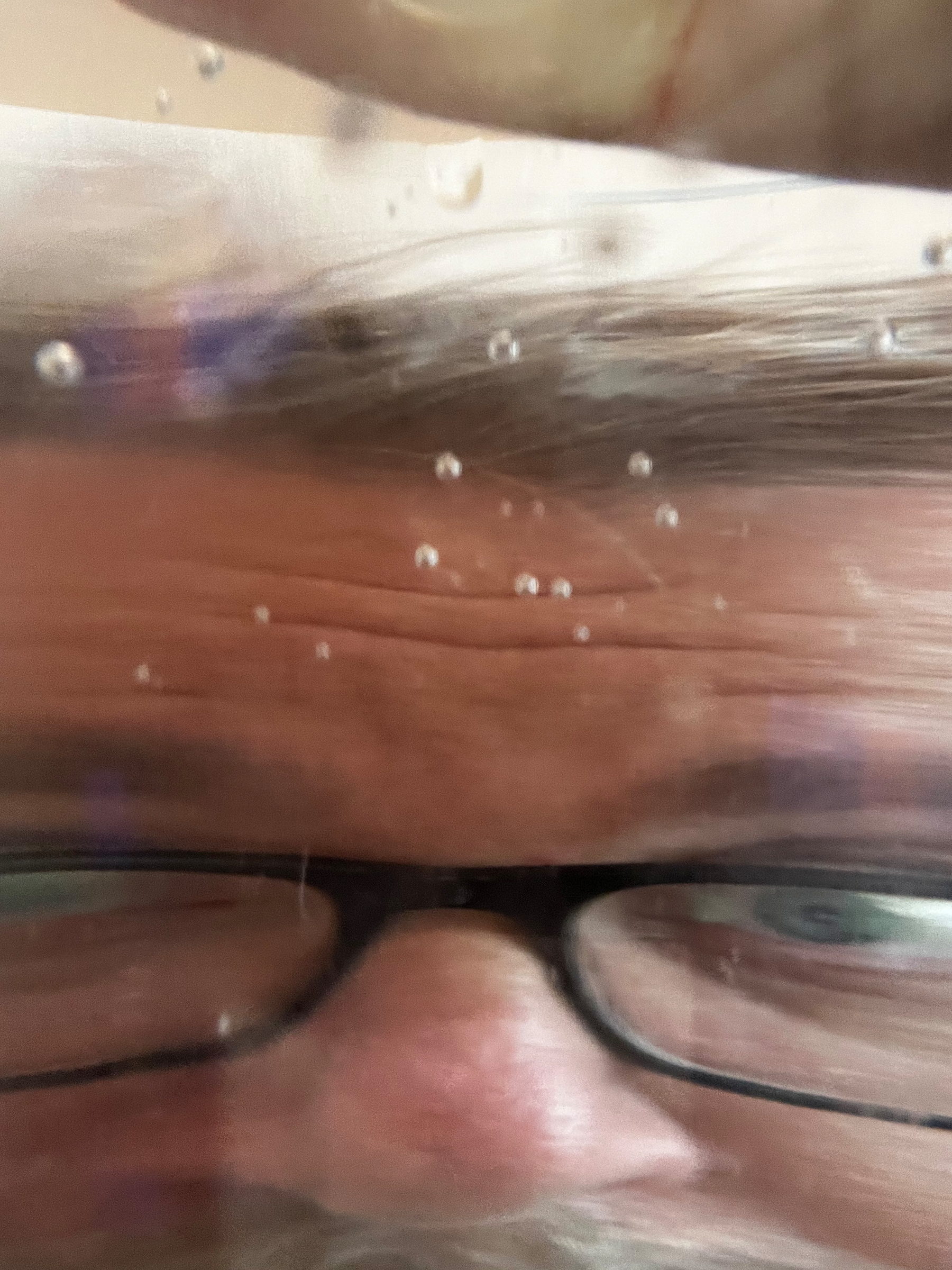 A close-up view of a person's face with glasses, partially obscured by water and bubbles.
