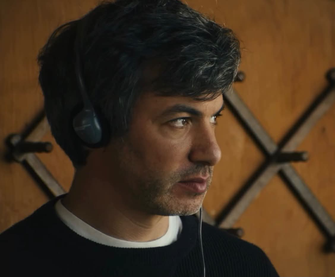 Nathan Fielder from the trailer for his new documentary with headphones on looking slightly disgusted and skeptical towards someone who’s speaking.