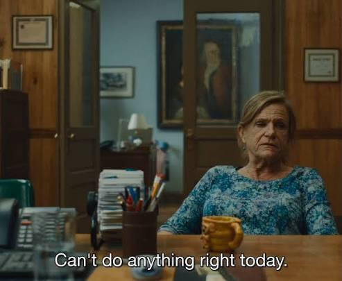 Screengrab from Widow’s Bay showing Rosemary (played by Dale Dickey) sitting at a desk with a stack of papers and a mug, while a caption reads, Can't do anything right today.