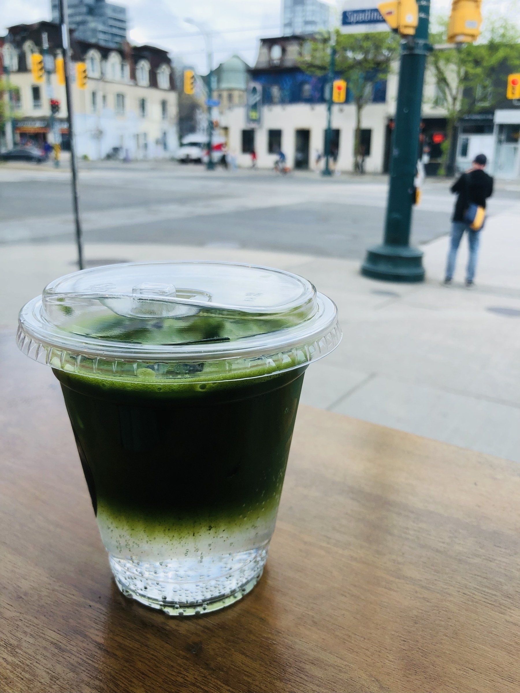 Matcha with tonic water in a transparent cup on a table looking at the corner of Nassau and Spadina in Toronto.