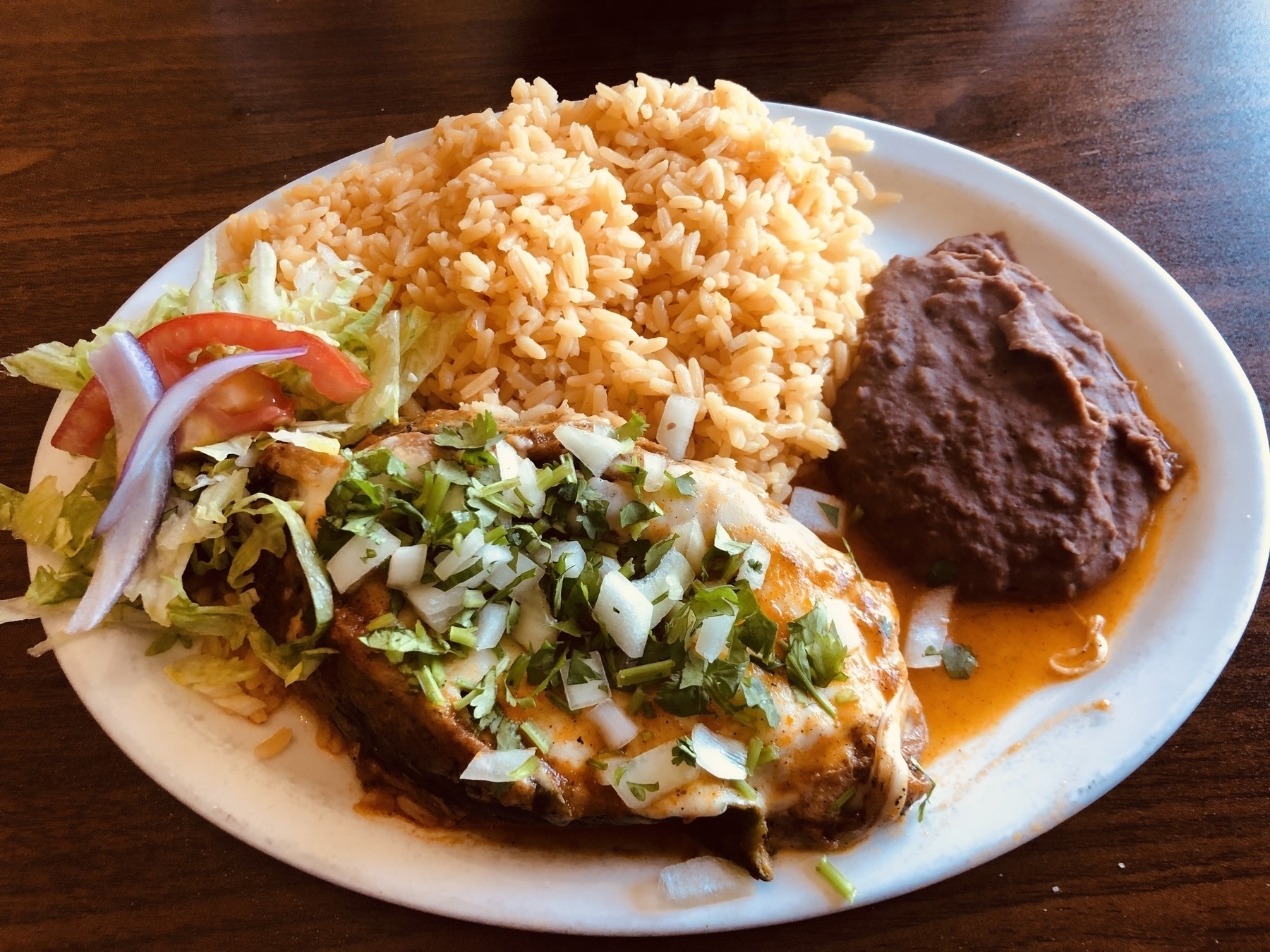 A chile rellenos with rice, a small salad and refried beans.