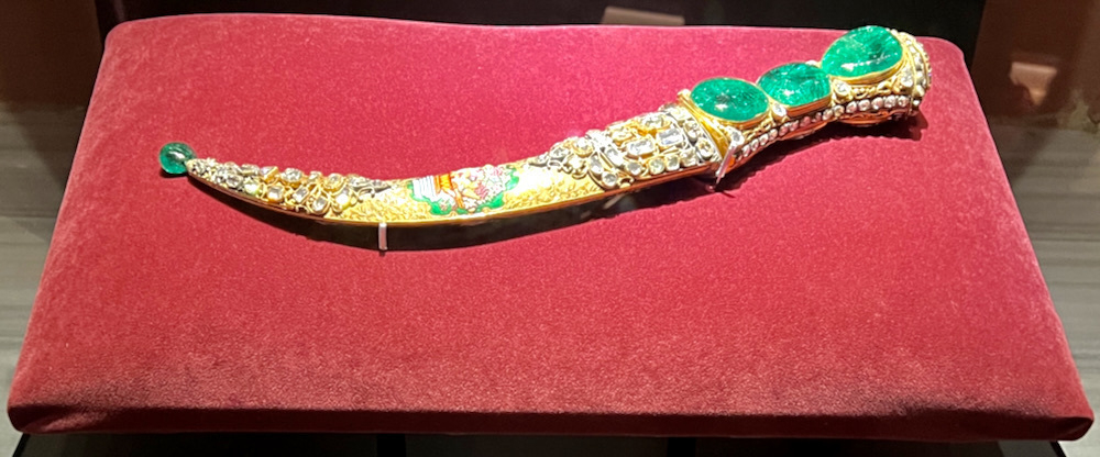 The gold filagreed curved Topkapi dagger with its three enormous emeralds on the hilt, sitting on a red cushion