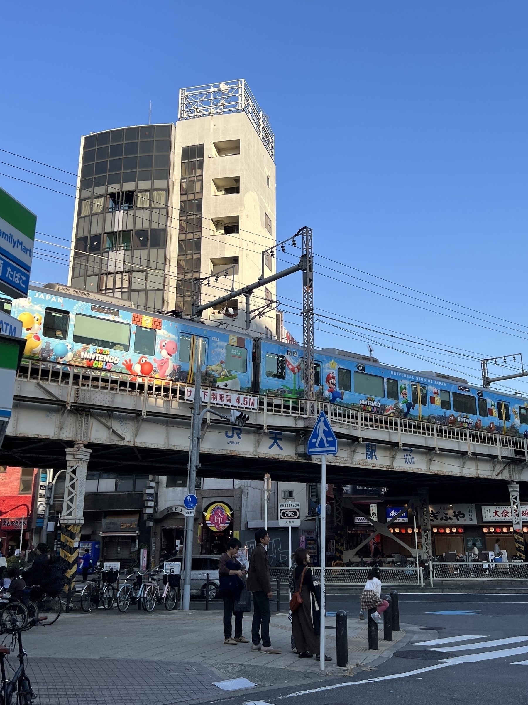 Colourful JR train with SUPER NINTENDO WORLD wrap passes over an Osaka intersection