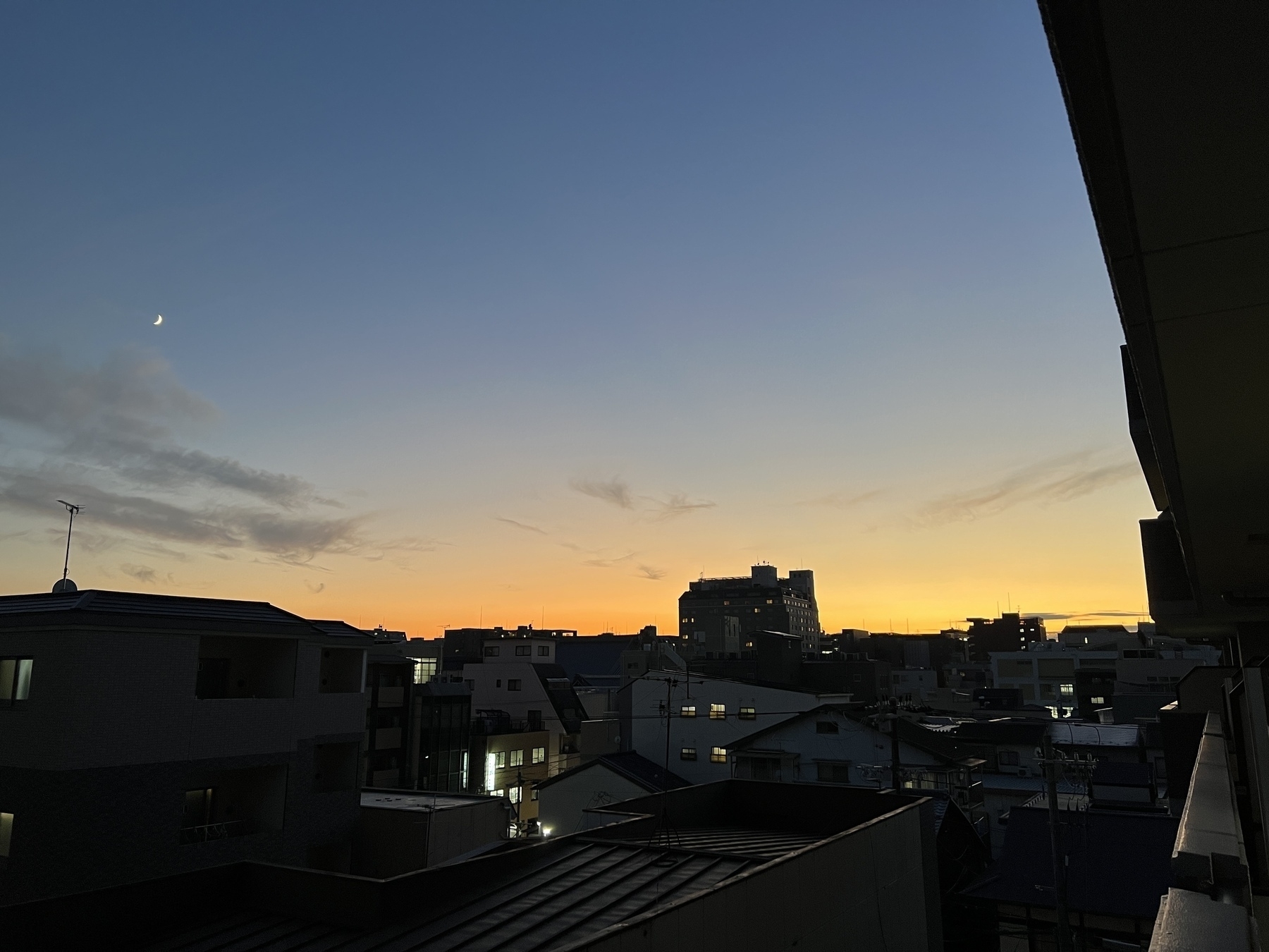 Sunset from a mid rise building balcony. A crescent moon is crisply visible in the sky