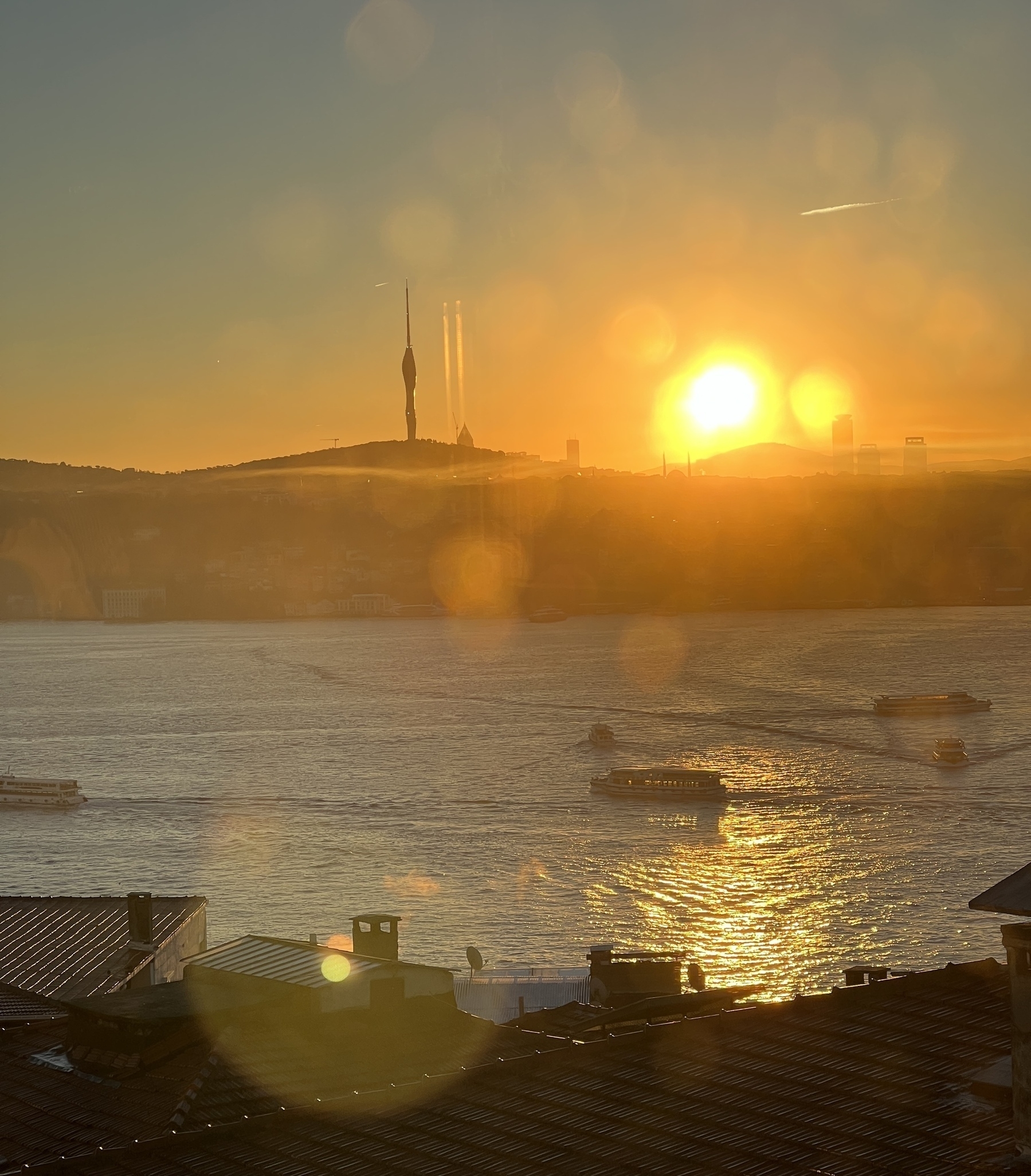Çamlıca Tower backlit by the sunrise across the water. Various ships and ferries pass through 