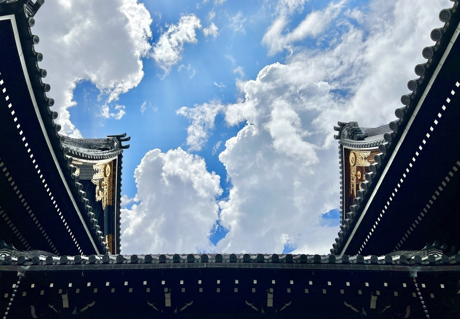 Between two temple eaves with shining brass details, the sky is filled with highly defined puffy white clouds that look like they are illustrated