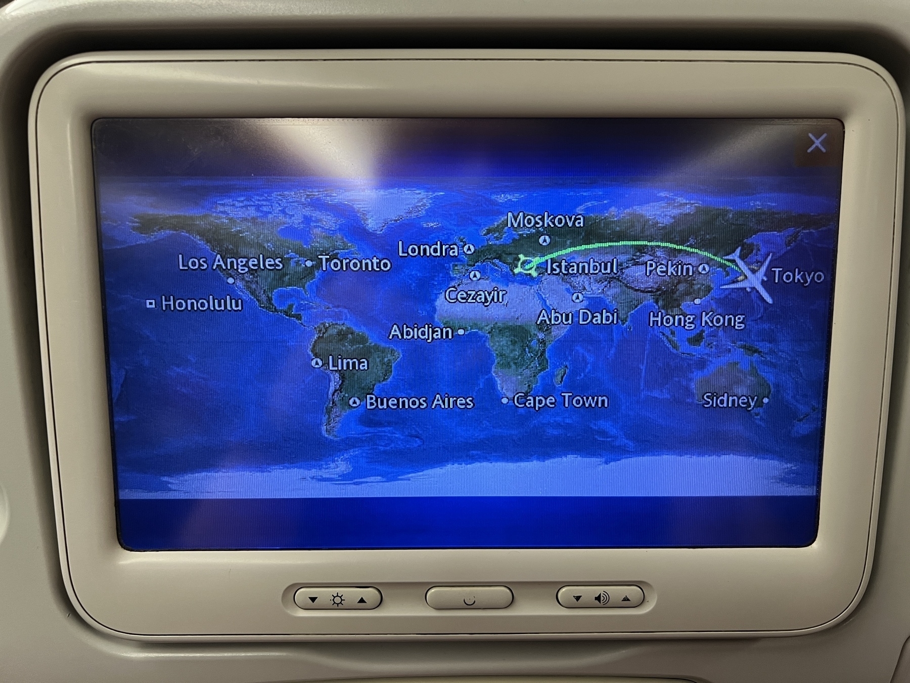 Photo of a back-of-seat monitor displaying a map of the world with a plane icon in Tokyo and destination icon in Istanbul, and a flight path arcing north with Novosibirsk at the top