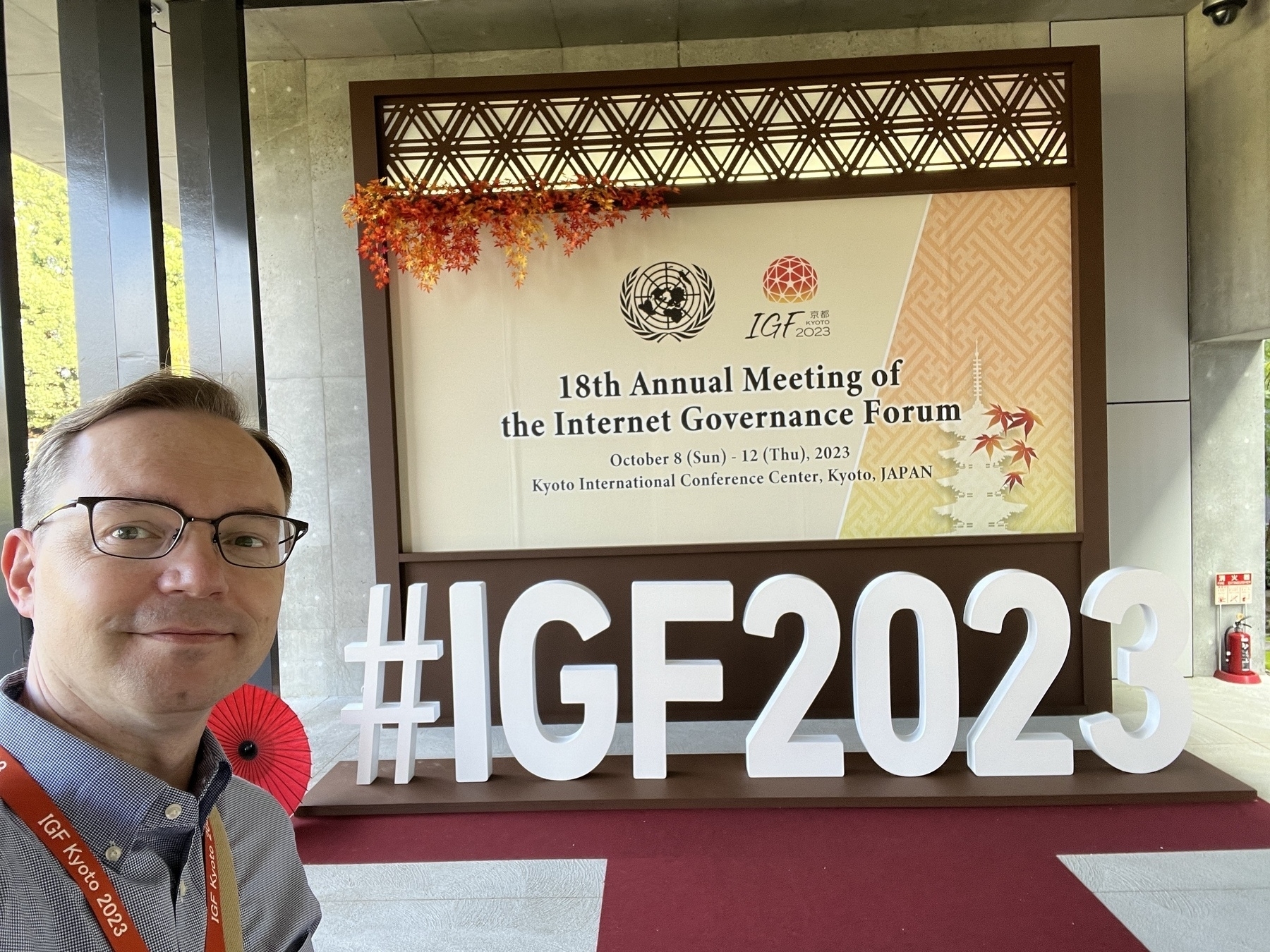 Chad selfie in front of the entrance to the Internet Governance Forum where there is a giant #IGF2023 hashtag