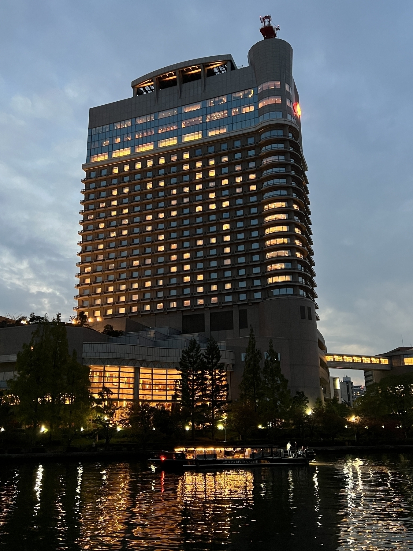 Early evening the Imperial Osaka Hotel is lit up. Below is the river in the foreground with a dinner boat passing by